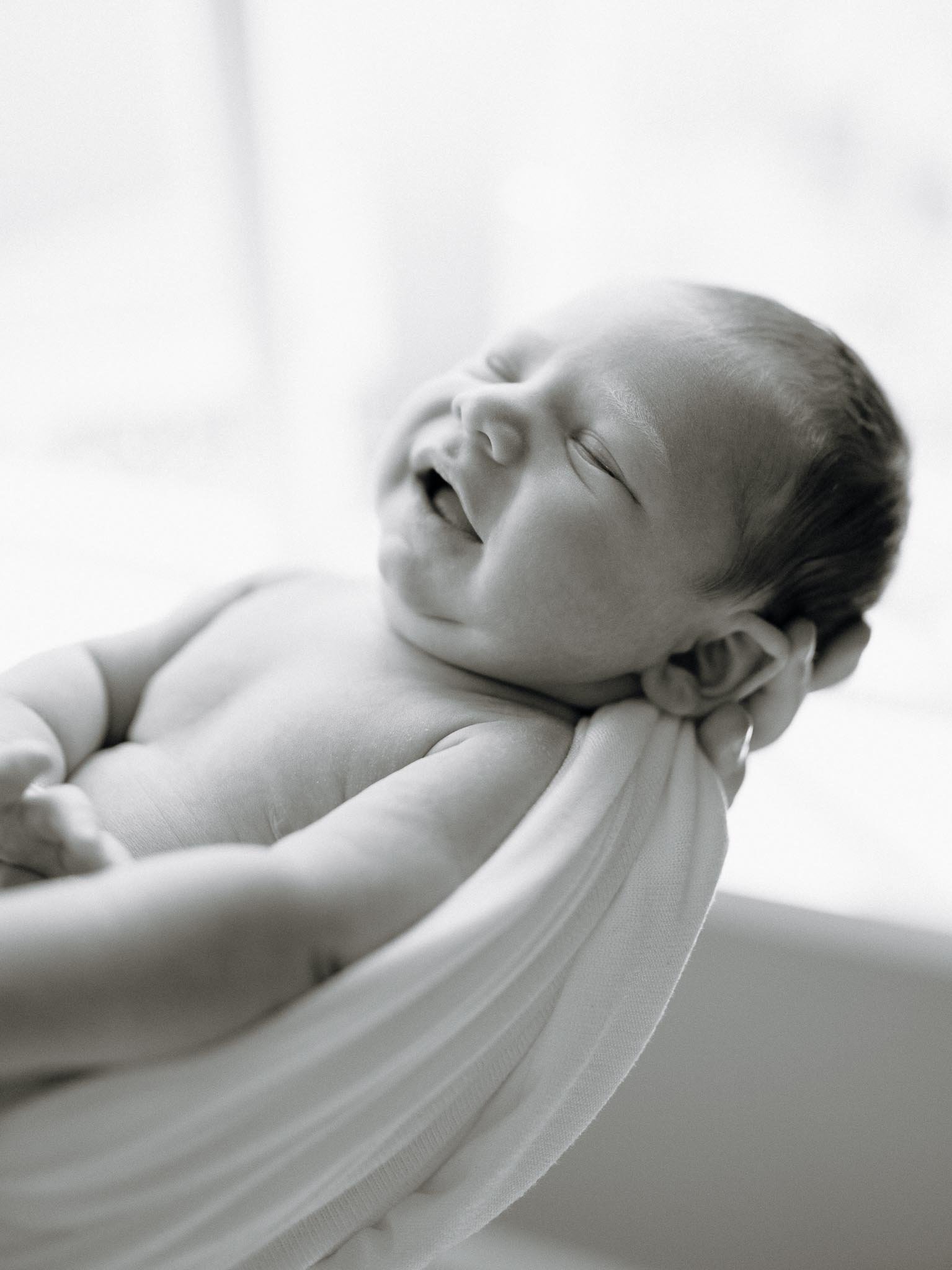Svart hvitt bilde av en nyfødt baby som holdes opp mot lyset. 