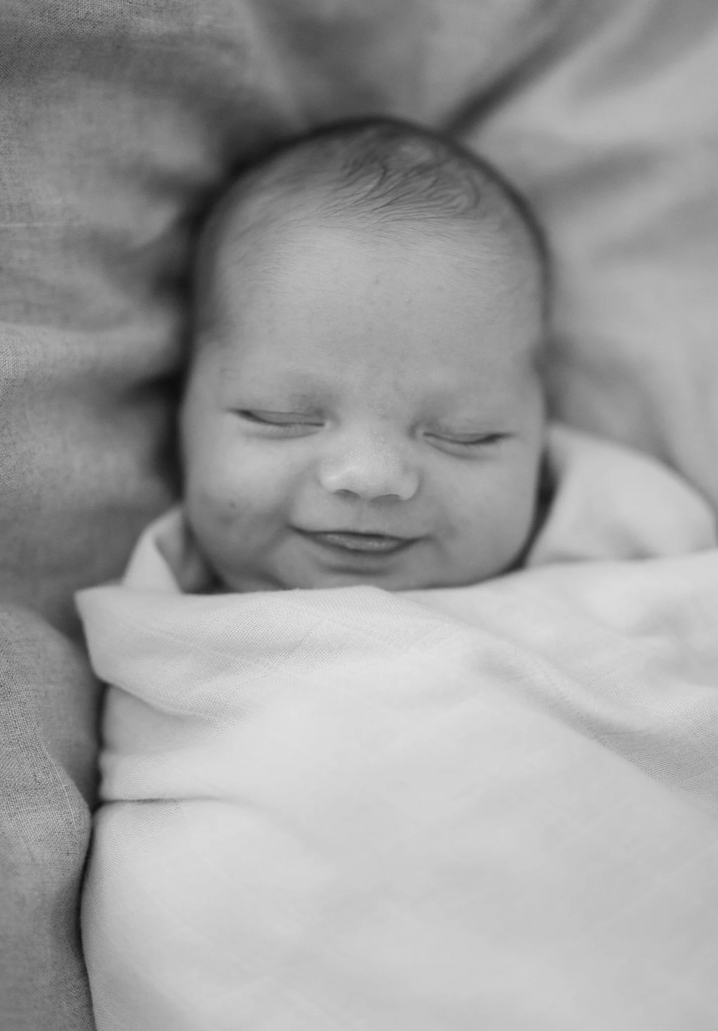 Sort-hvitt bilde av en sovende baby som ligger på en myk overflate, med øynene lukket og et rolig ansiktsuttrykk.