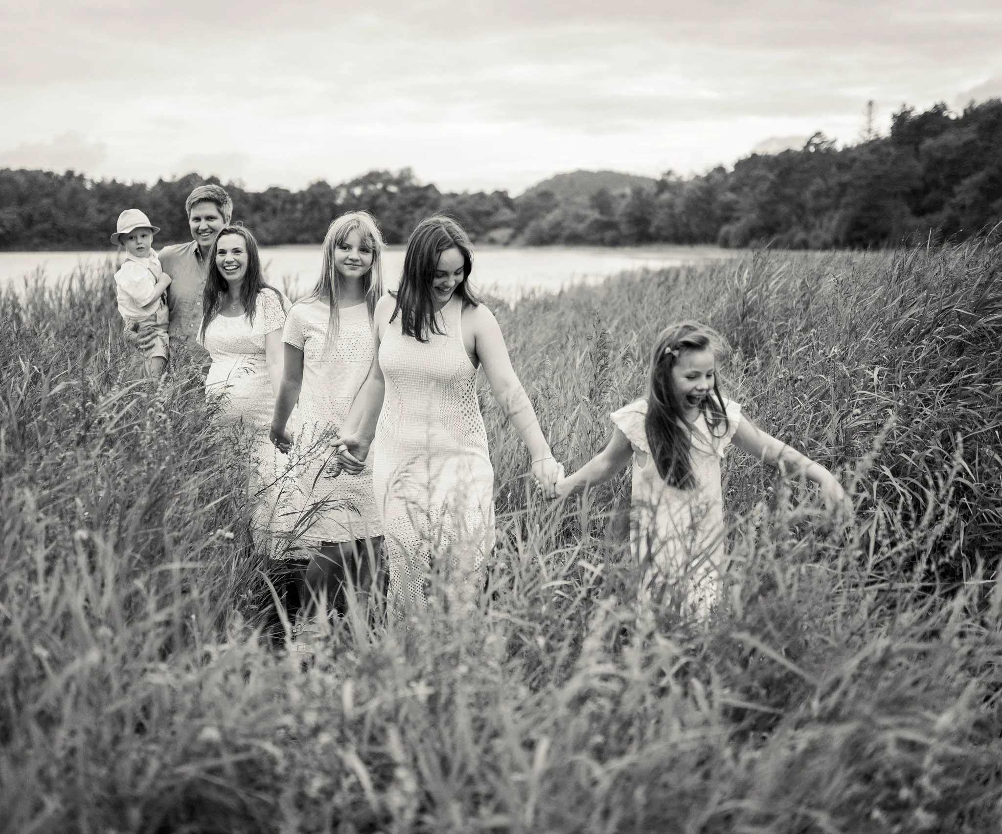 Familiefotografering i en eng med strå. Holder hverandre i hendene og løper og smiler.