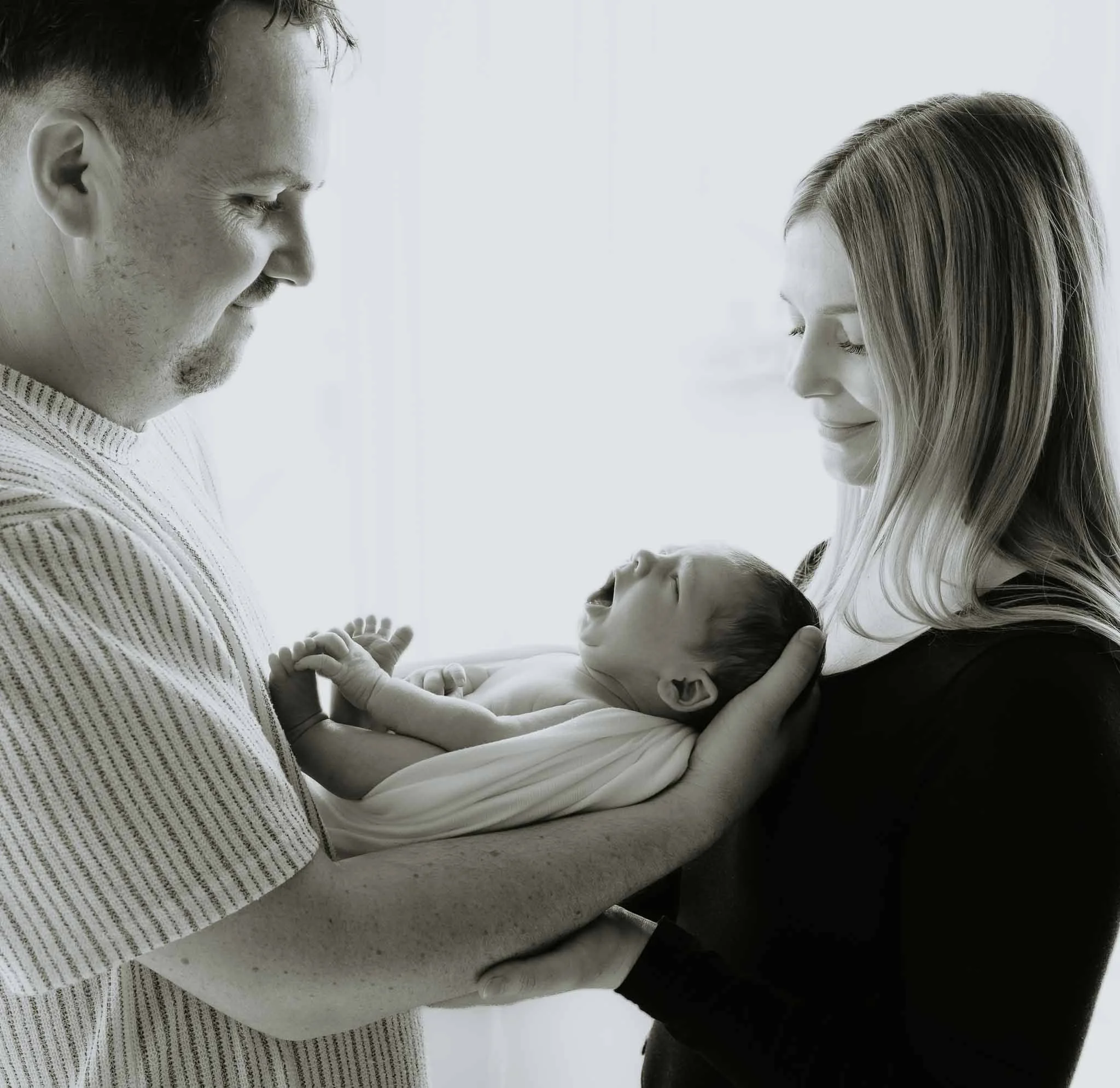 Mor, far og nyfødt baby. Far holder babyen. Ser på han og smiler. 
