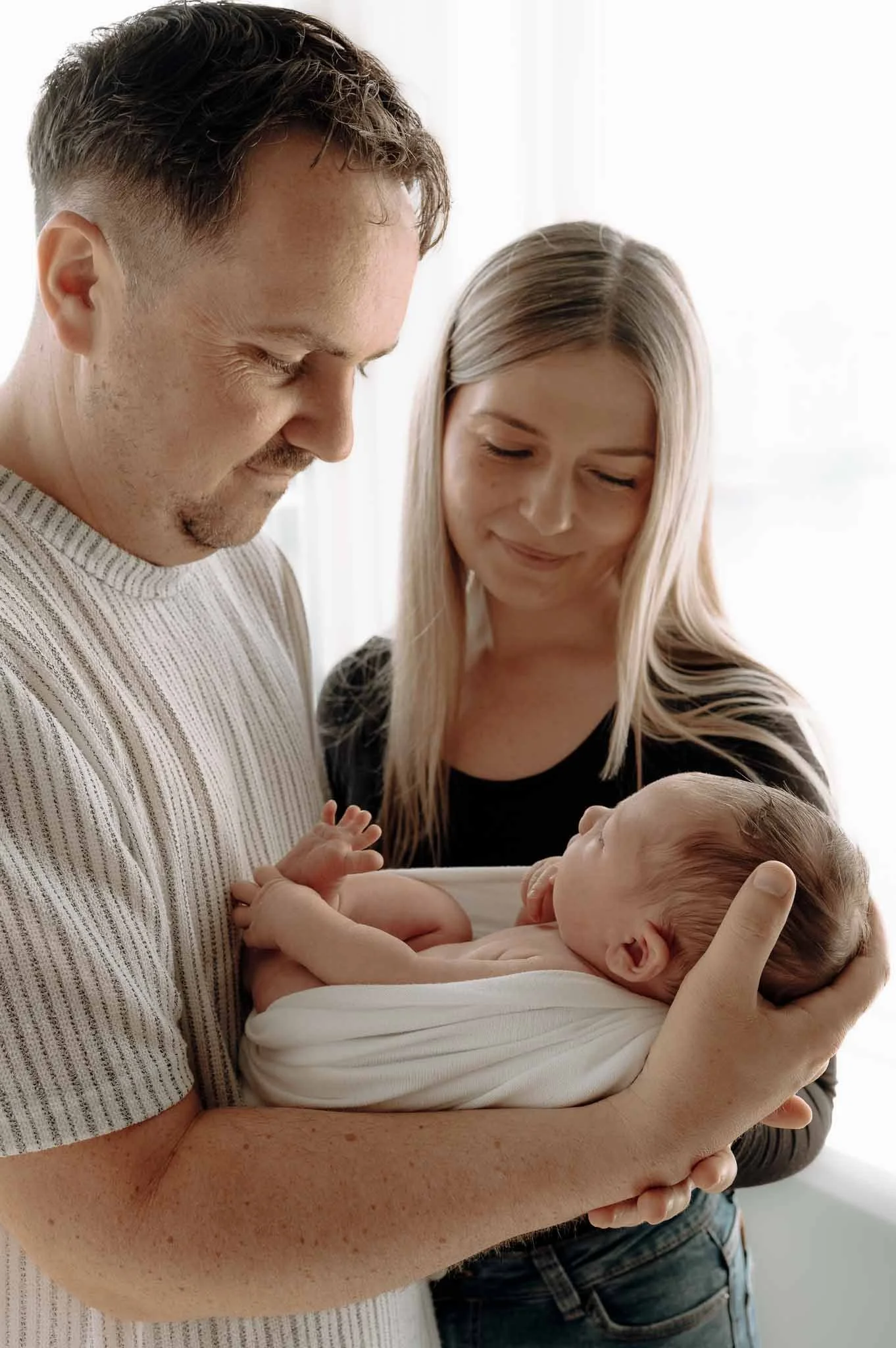 Mor, far og nyfødt baby. Far holder babyen. Ser på han og smiler. 