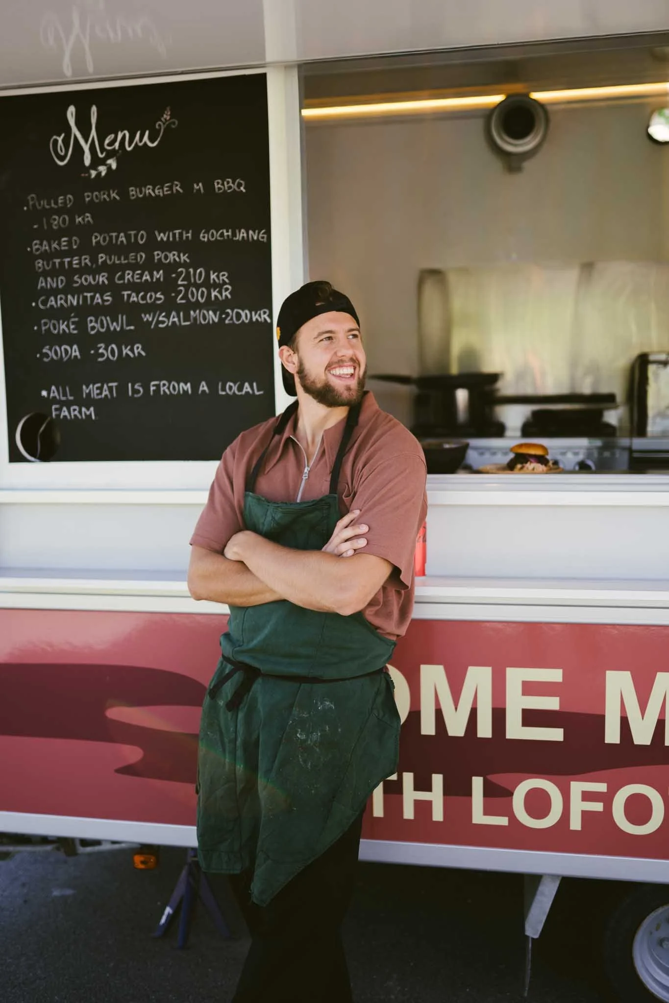 Kokk står utenfor food truck. Smiler. 