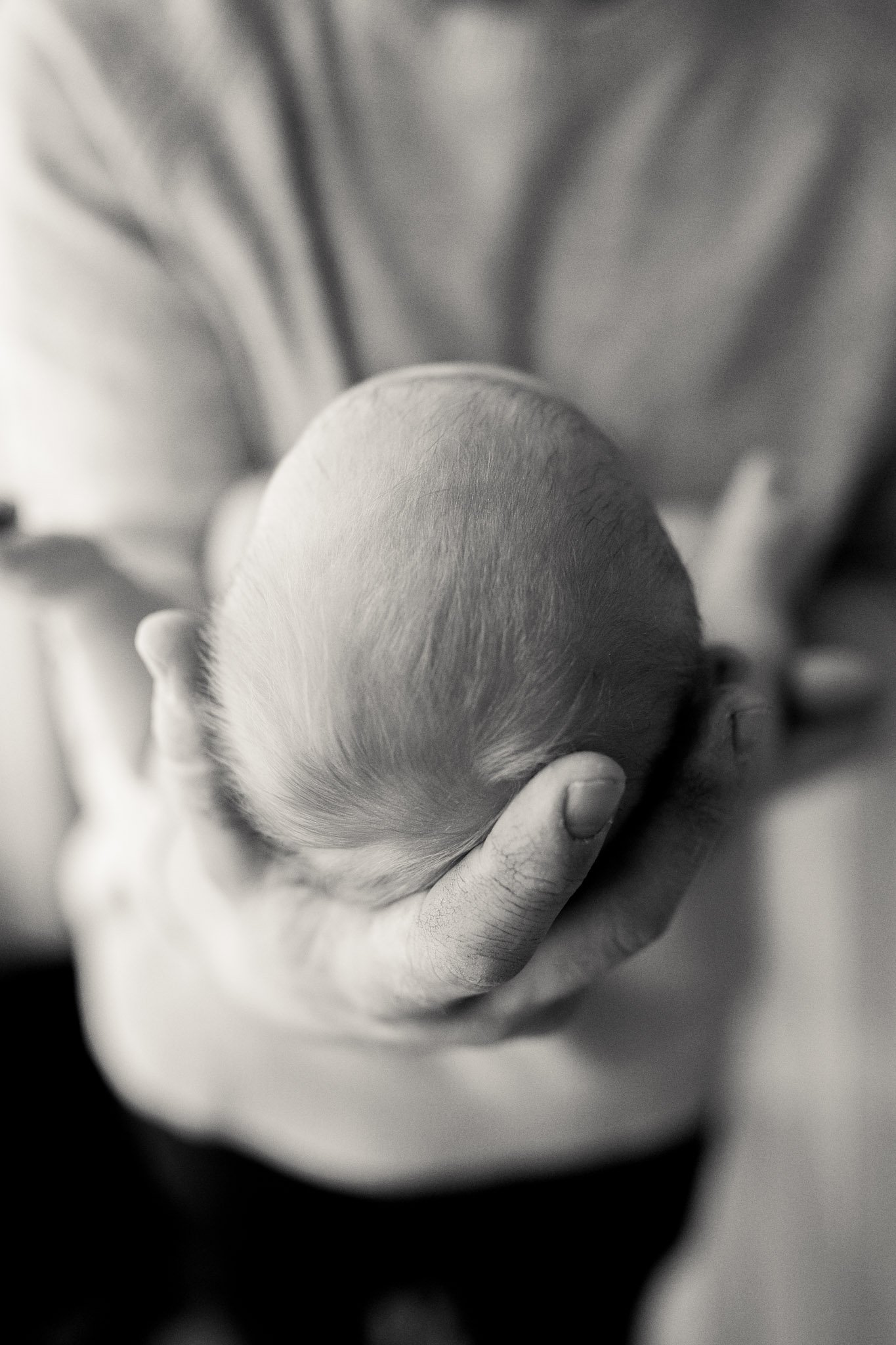 En person holder forsiktig et nyfødt babyhode, svart-hvitt foto.