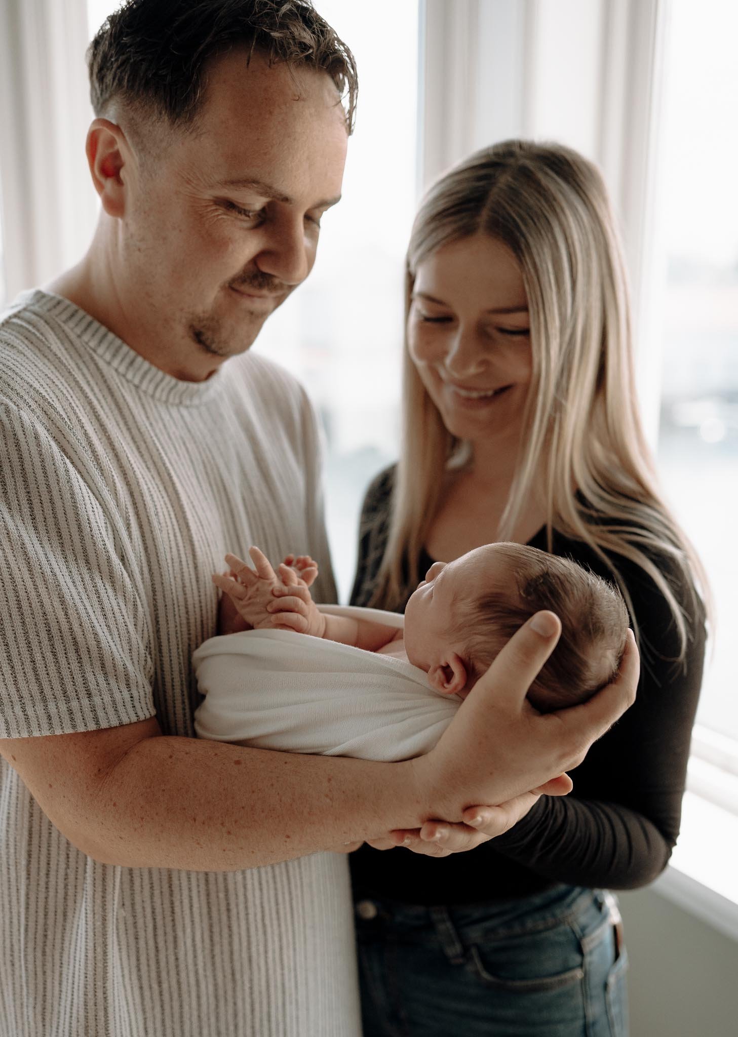 Mor, far og nyfødt baby. Far holder babyen. Ser på han og smiler. 
