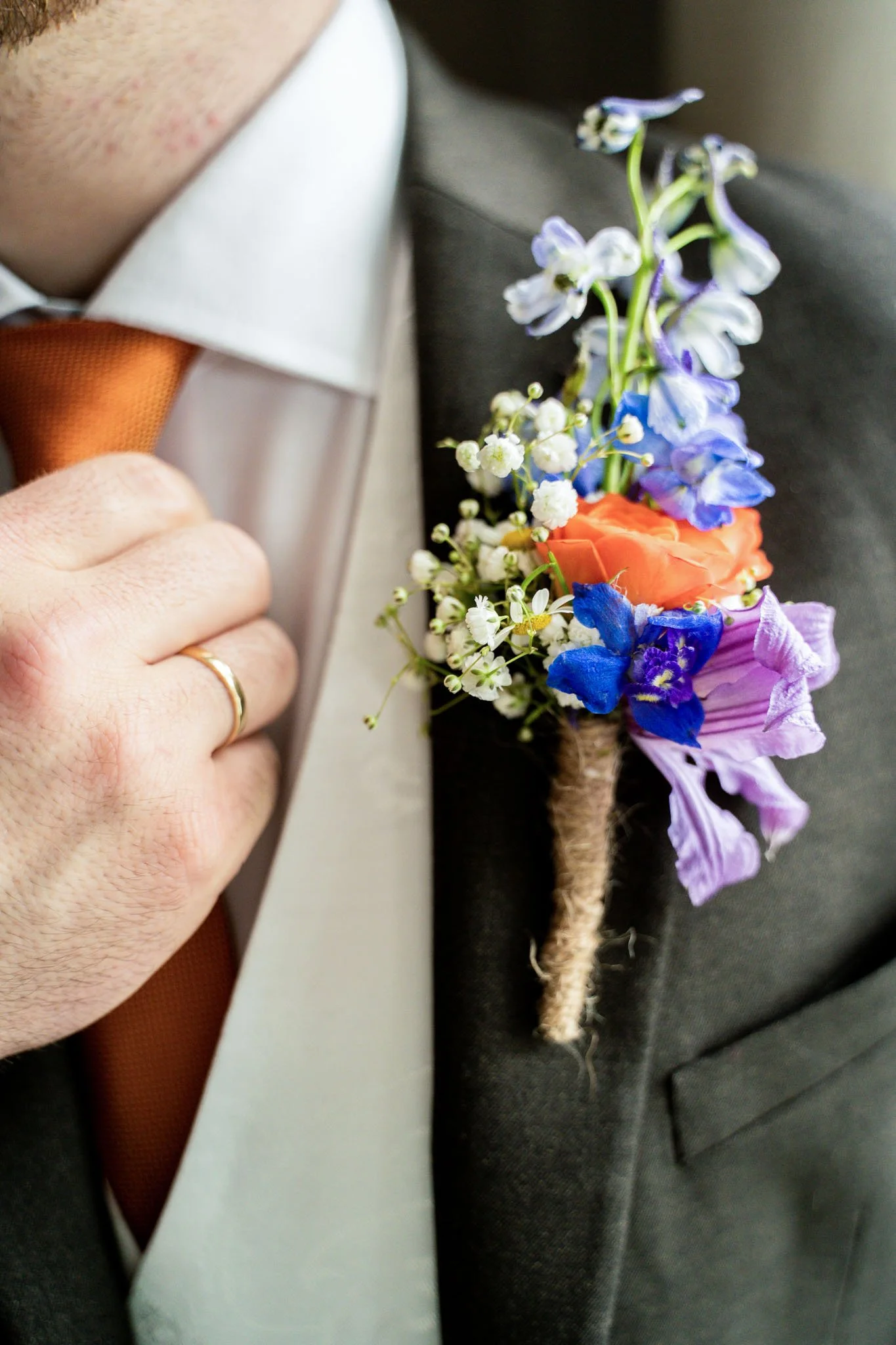 En person i formell antrekk med hvit skjorte, grå jakke og oransje slips, med en bukett blomster festet på jakkeslaget.
