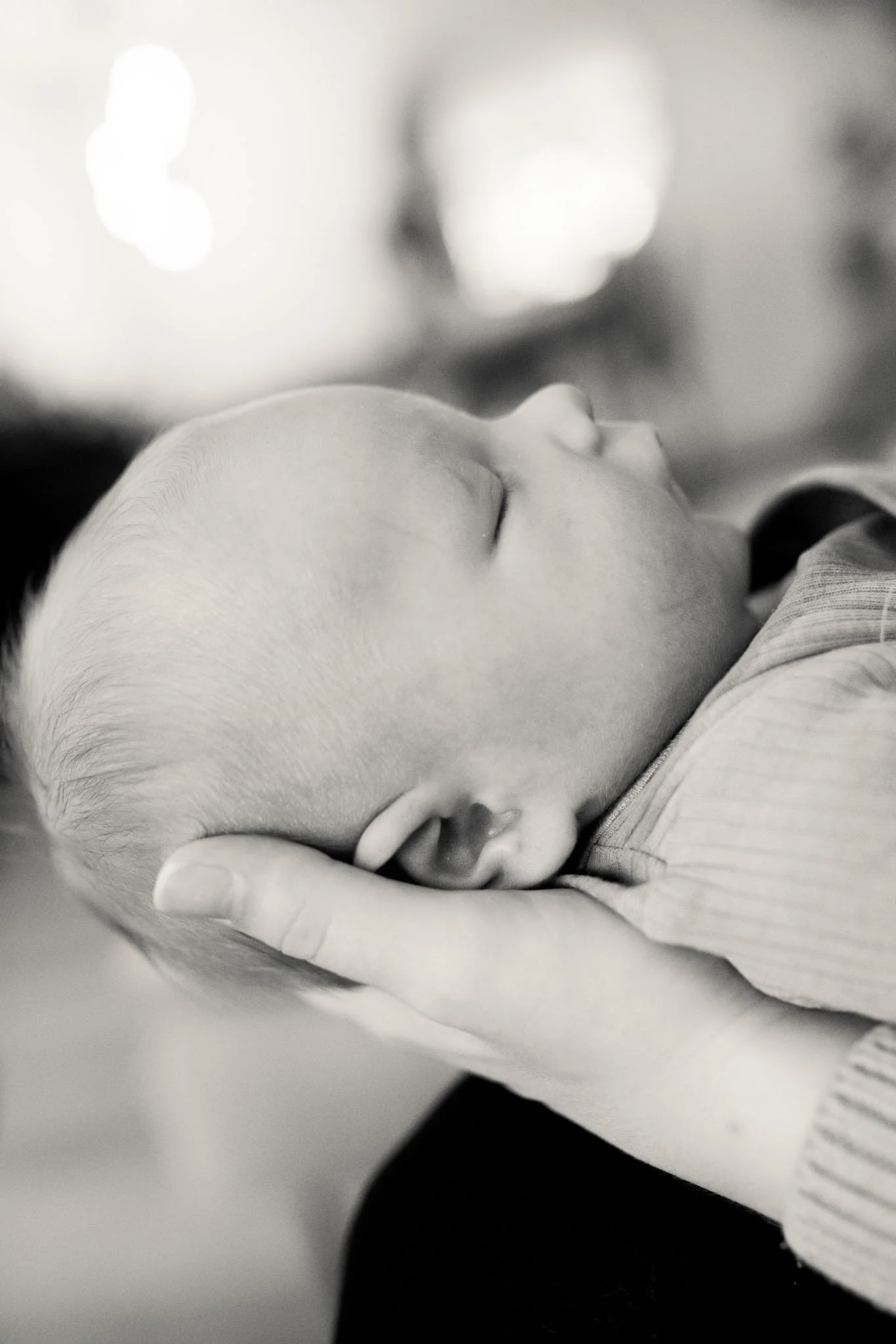 Et nært, svart-hvitt bilde av en baby som sover, heltes i en voksenhånd.