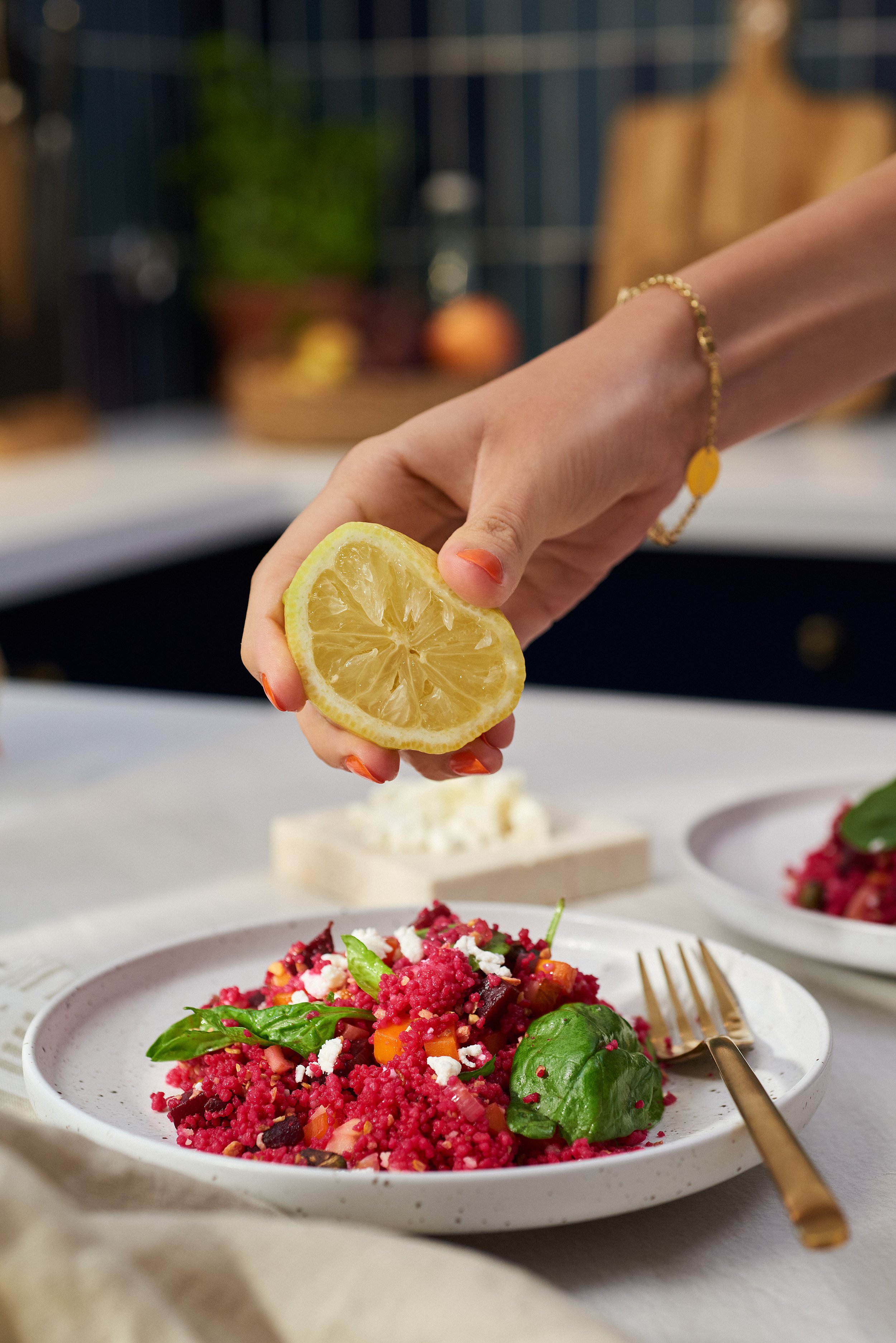 A hand squeezing lemon over a colorful beet and vegetable salad on a white plate.