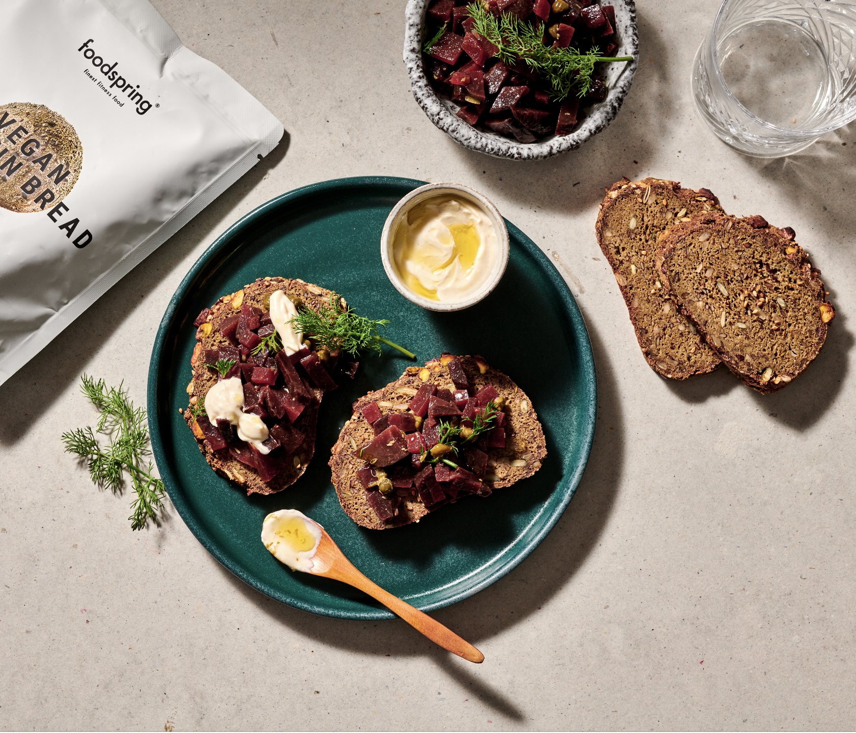Vegan rye bread slices topped with beetroot, garnished with dill and served with a dollop of vegan mayonnaise, on a green plate with a small bowl of vegan mayonnaise, a piece of beetroot salad, and a glass of water.