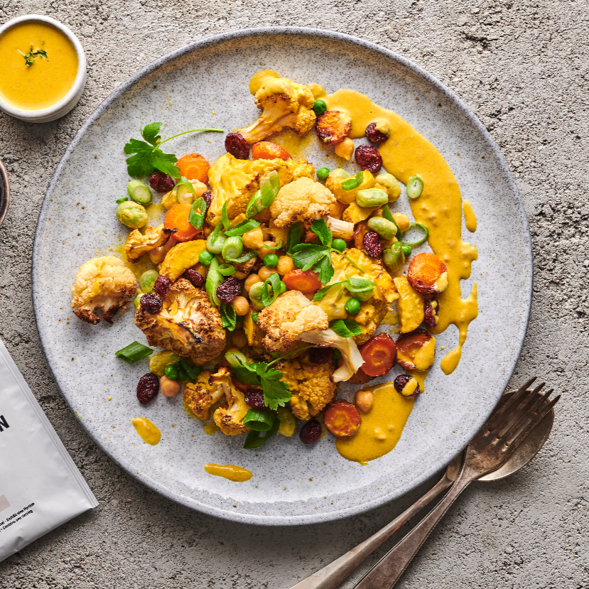 Roasted cauliflower and vegetables with yellow sauce and green herbs on a gray plate
