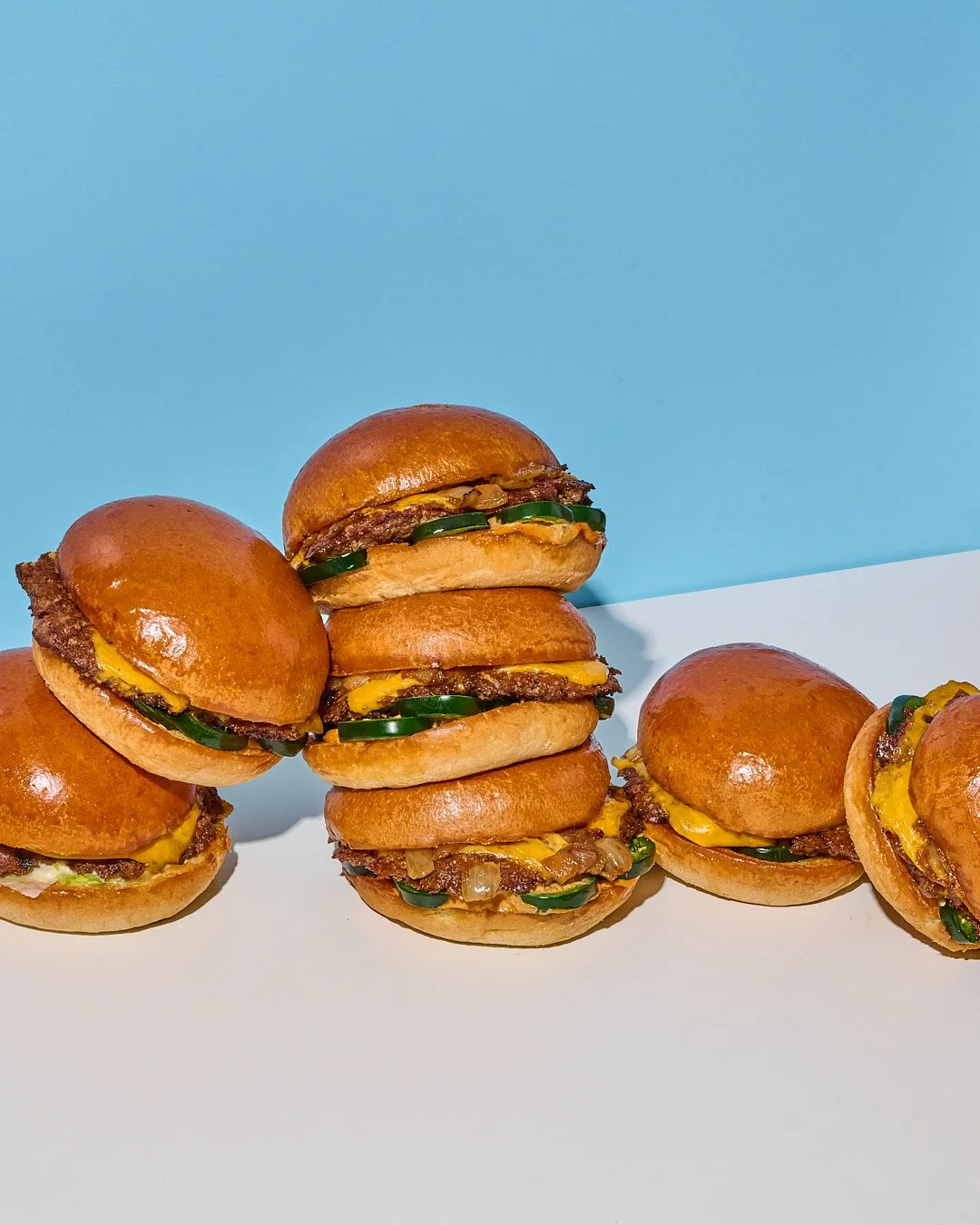Multiple cheeseburgers with pickles, onions, and mustard on a blue and white background.
