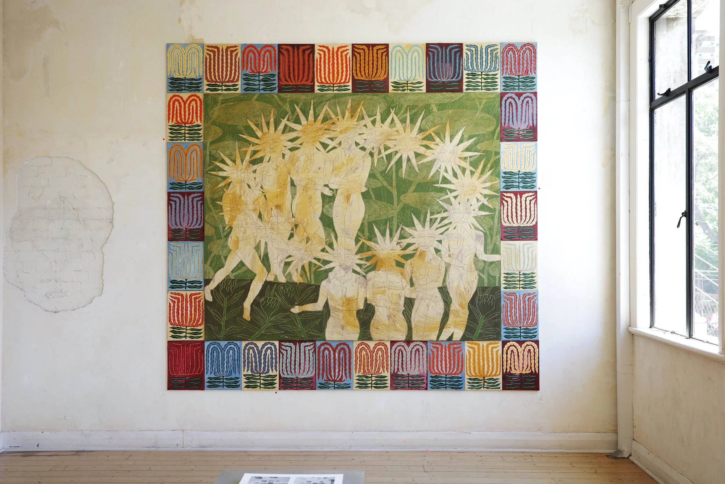 A large colorful painting on a gallery wall featuring abstract figures surrounded by starburst shapes, with a decorative border of geometric patterns in multiple colors.