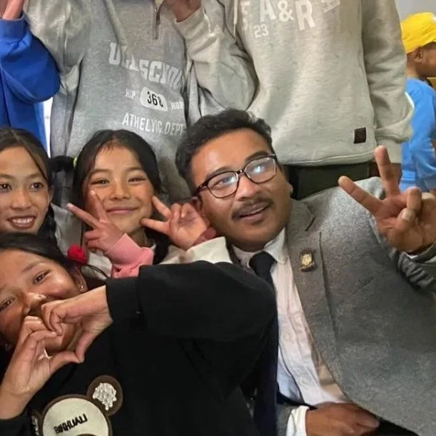 Group of children and an adult taking a selfie together, making peace signs and smiling.