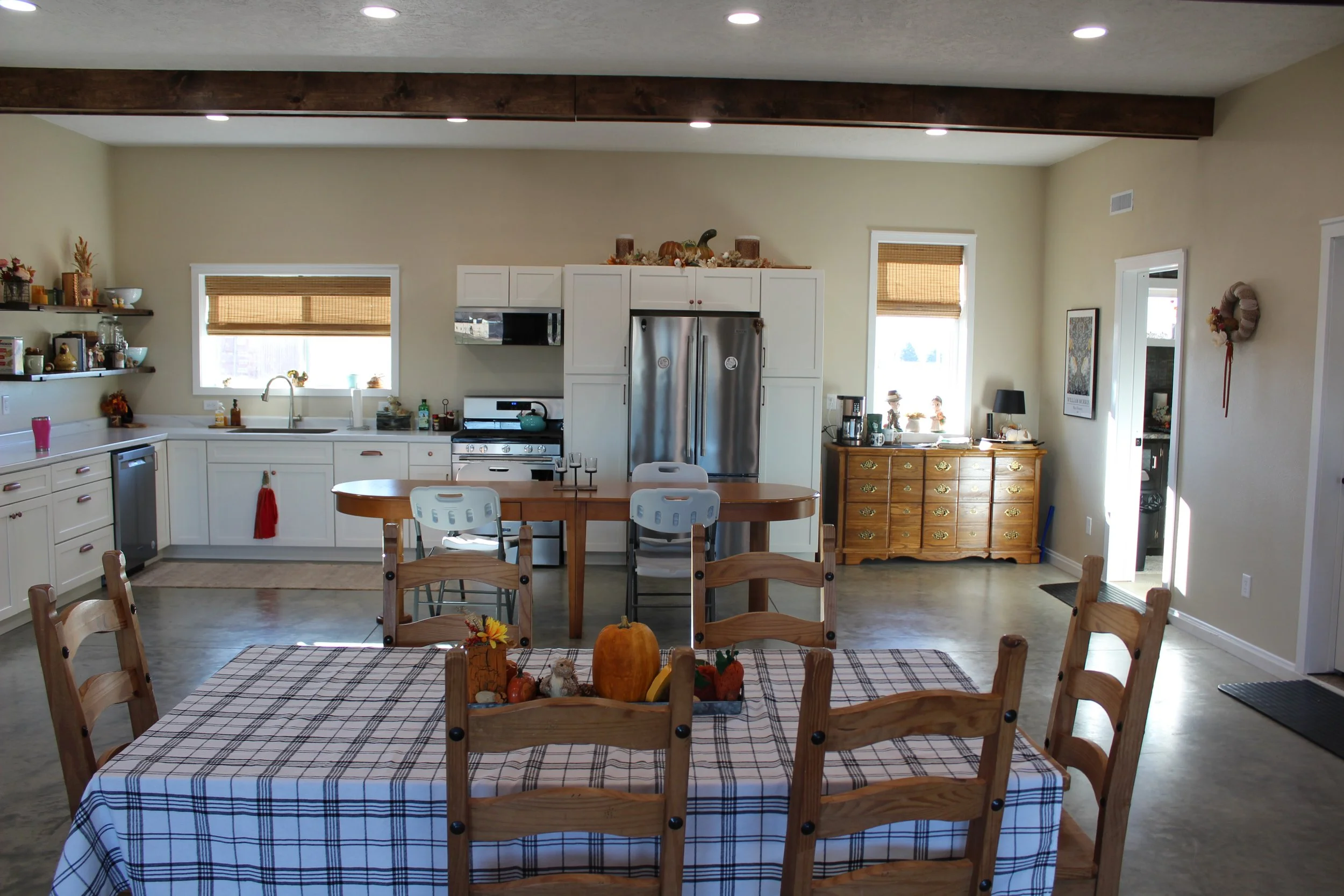 Open concept kitchen and dining area with a wooden table and six chairs, decorated with fall-themed items, and kitchen with white cabinets, stainless steel appliances, and wooden accents, illuminated by recessed ceiling lights.