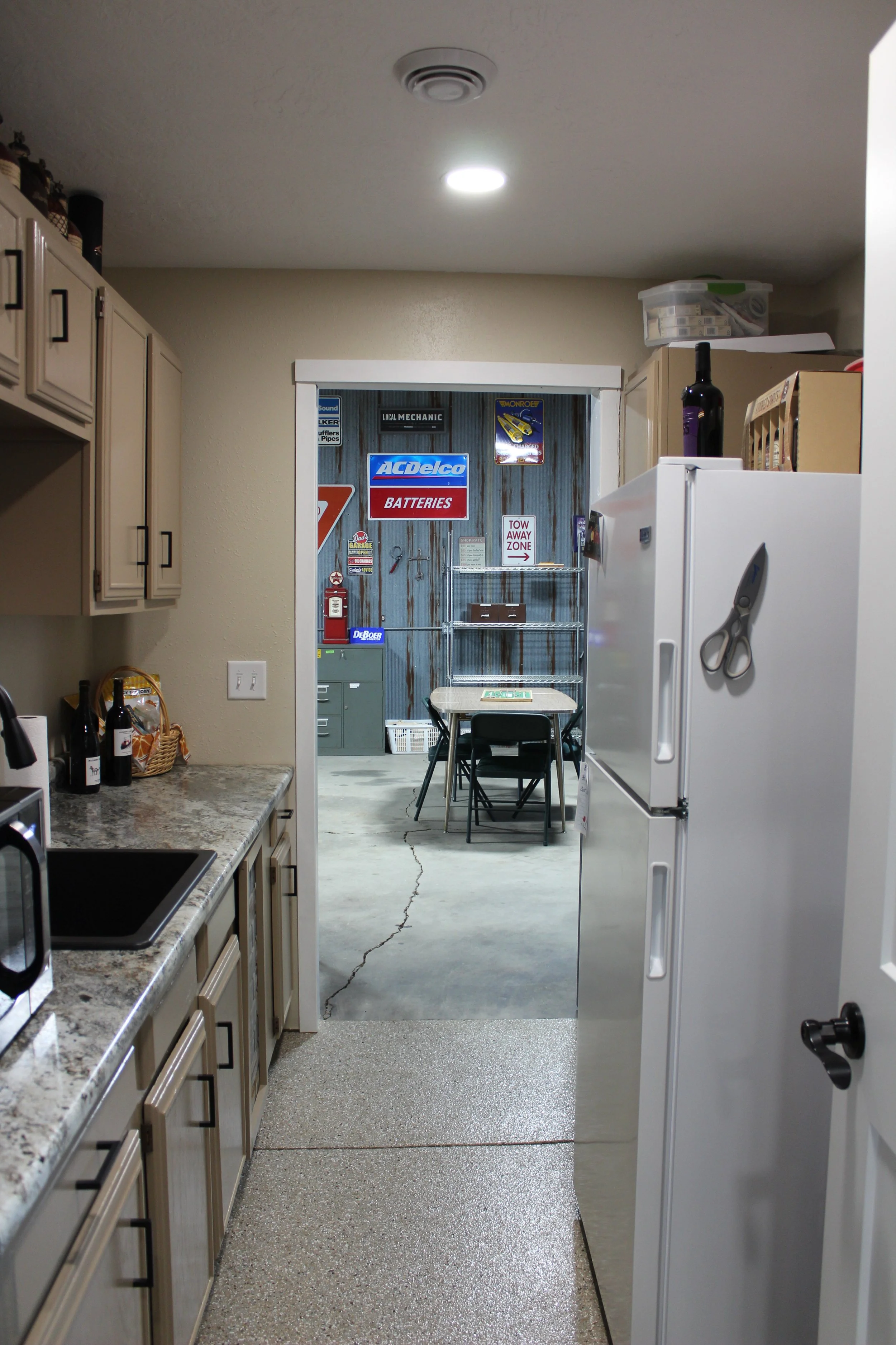 View from a kitchen looking into a garage or workshop area with signs, table, and chairs.