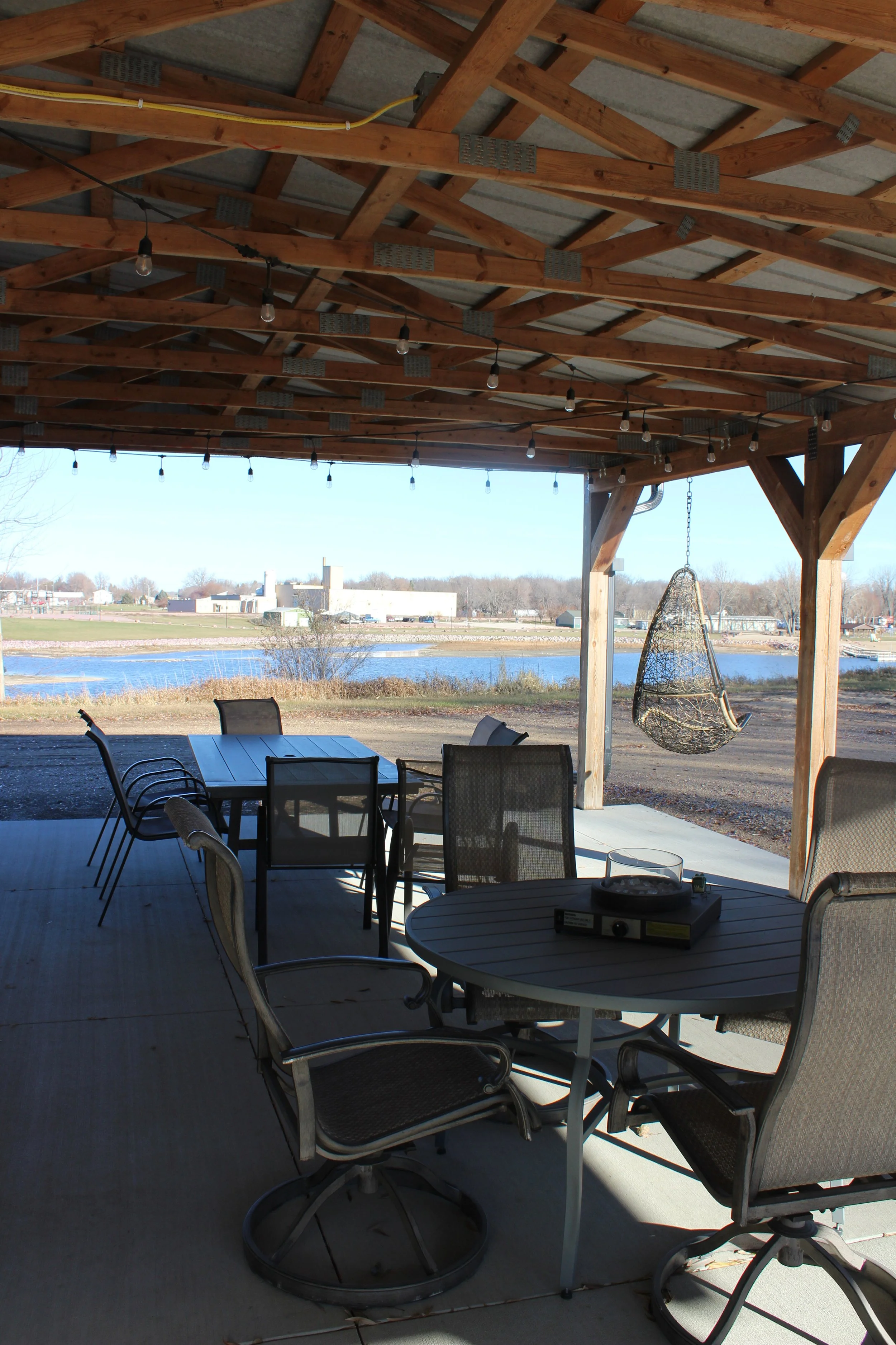 Outdoor covered patio with a wooden ceiling, string lights, patio furniture, and a view of a pond with grass and trees.