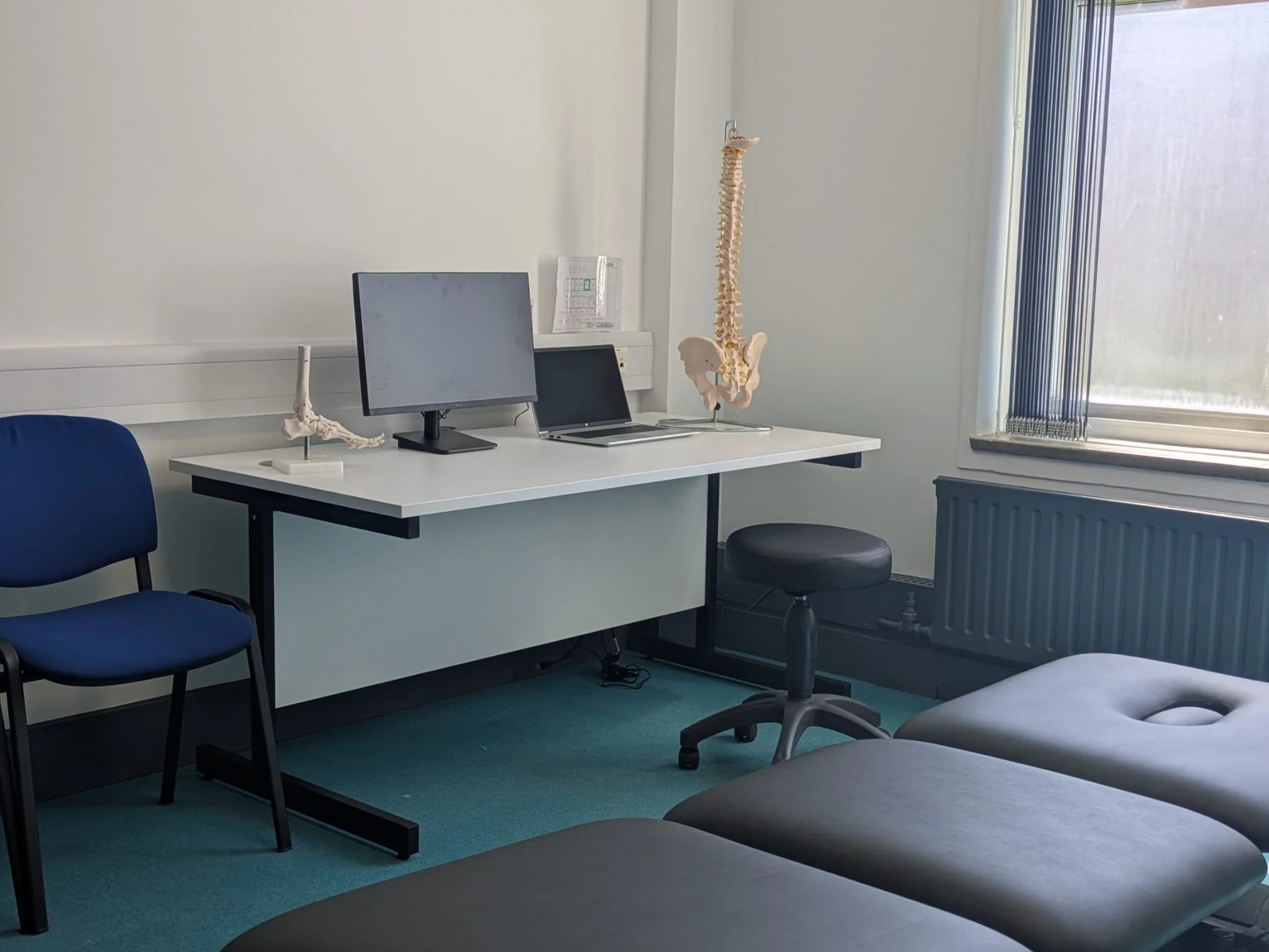 Physiotherapy treatment room featuring an desk, laptop, treatment bed for physio treatments
