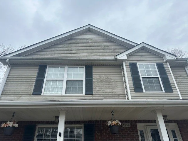 Front view of a two-story suburban house with beige siding, white trim, black shutters, and hanging flower baskets on the porch.