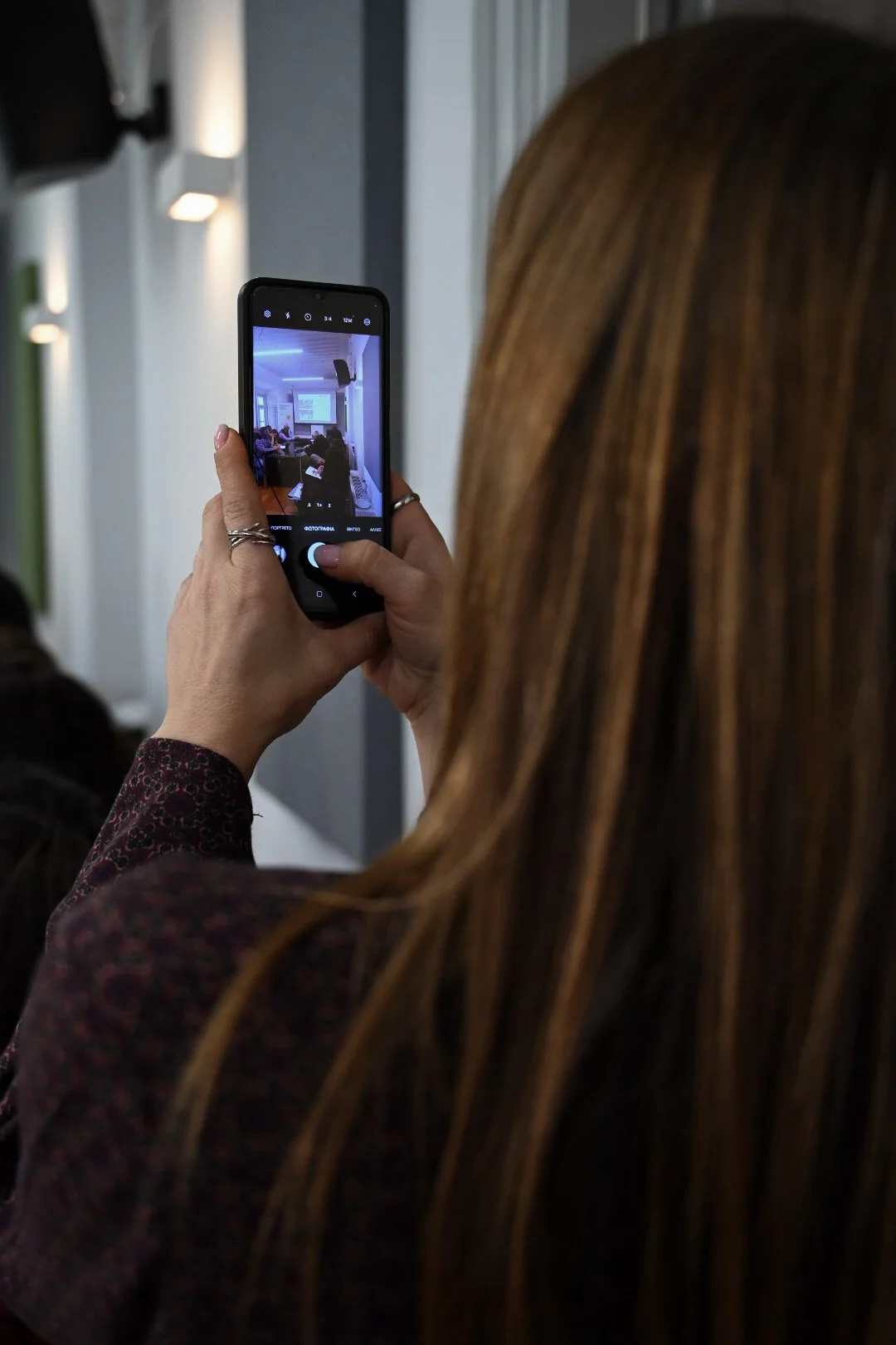 Person taking a photo of a classroom presentation with a smartphone during a meeting or lecture.