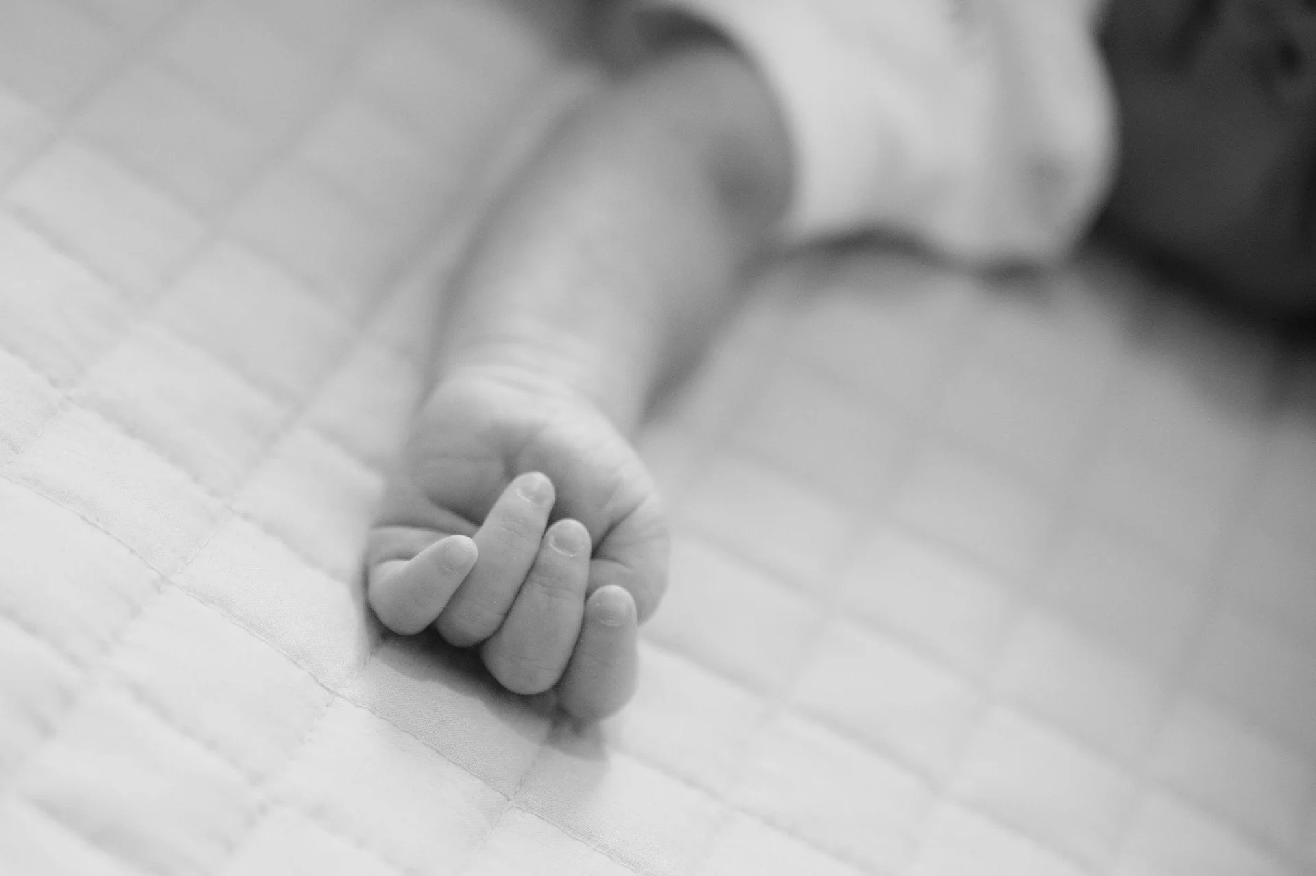 Close-up of a baby's hand resting on a soft surface.