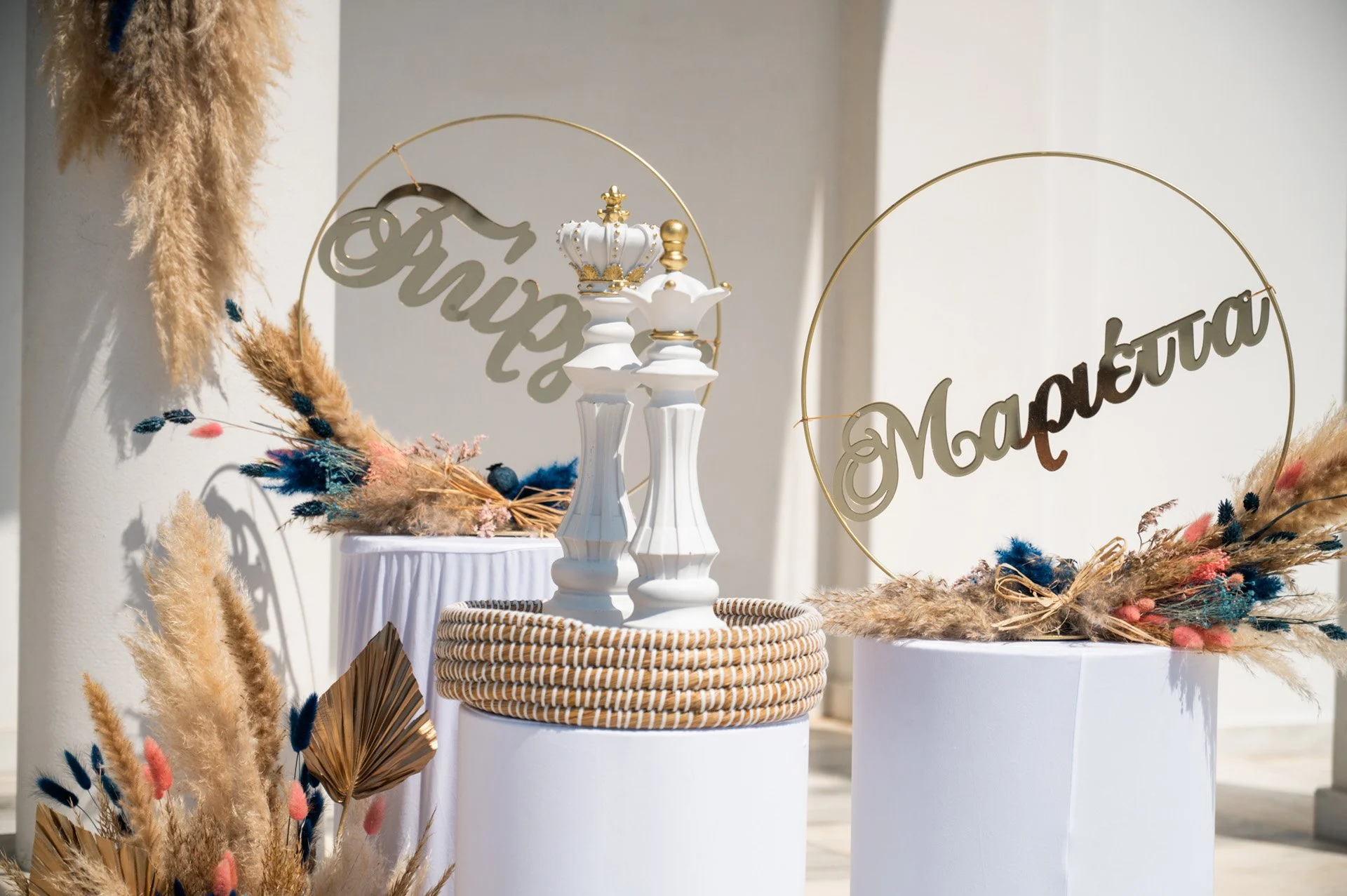 Decorative floral arrangements on white pedestals, with circular signs in gold with inscriptions in Cyrillic, and white figurines of candlesticks with crowns, against a neutral background.