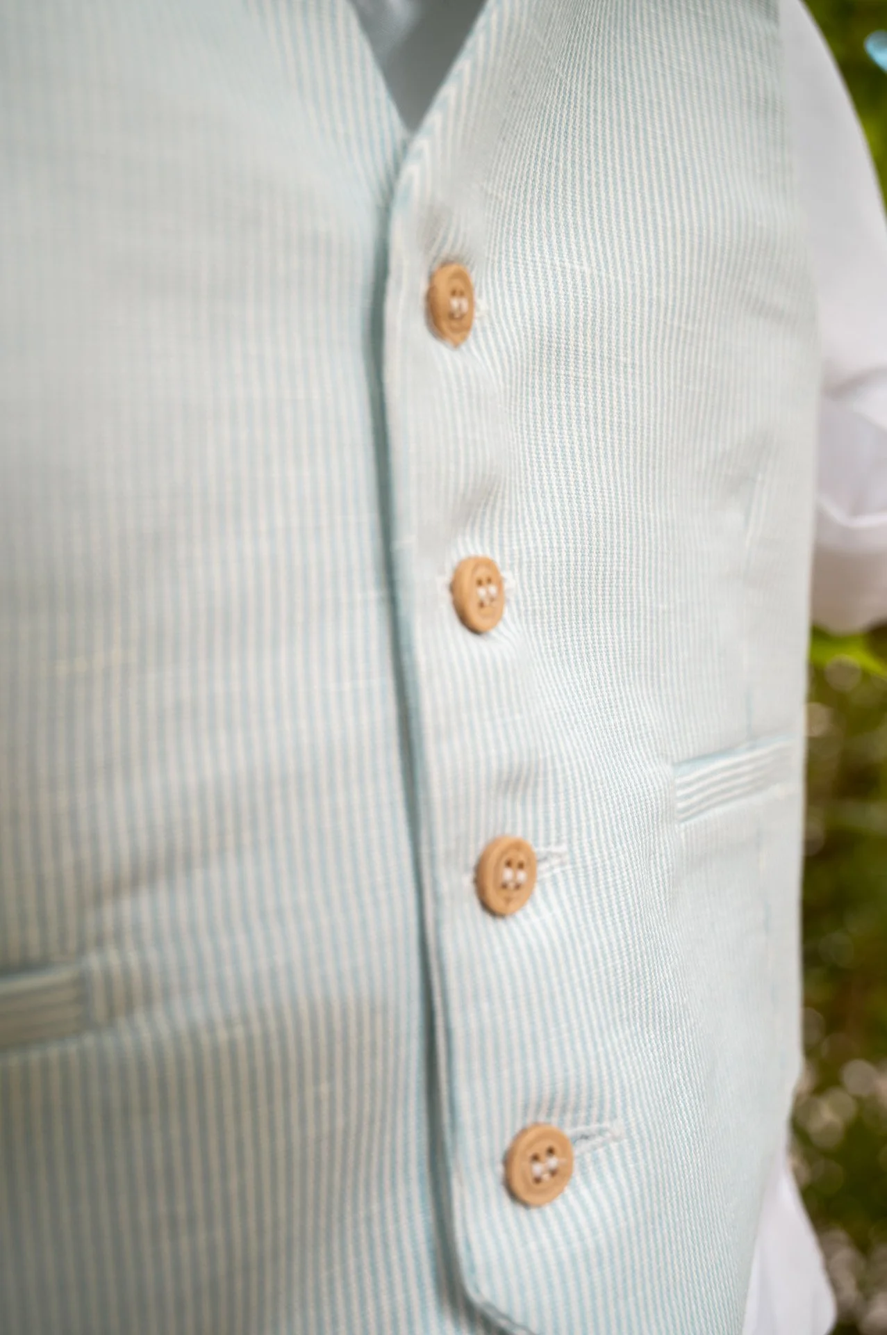 Close-up of a light blue and white striped vest with tan buttons, worn over a white shirt.