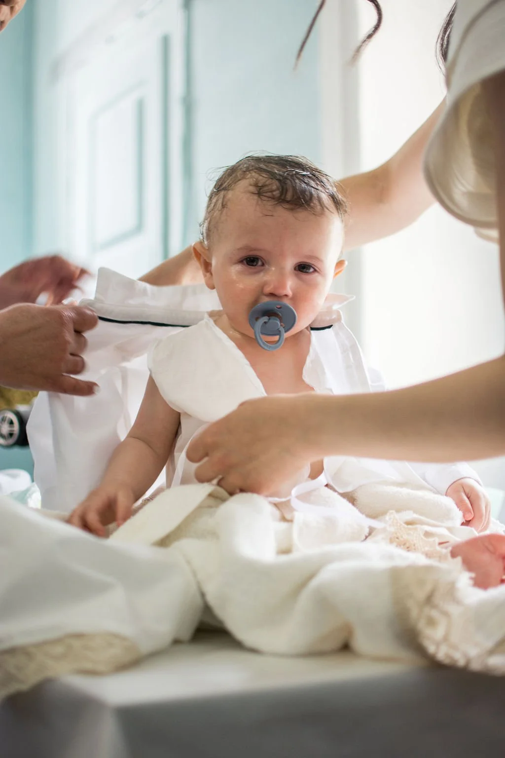 A young child with a pacifier getting medical care or examination in a hospital or clinic setting, with medical staff assisting.