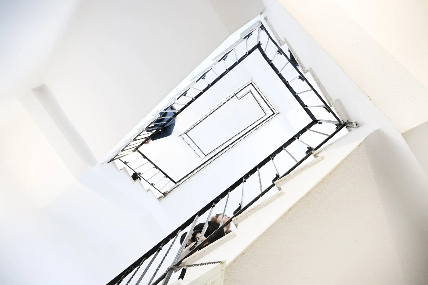 View looking up at a spiral staircase with black metal railings and white walls.