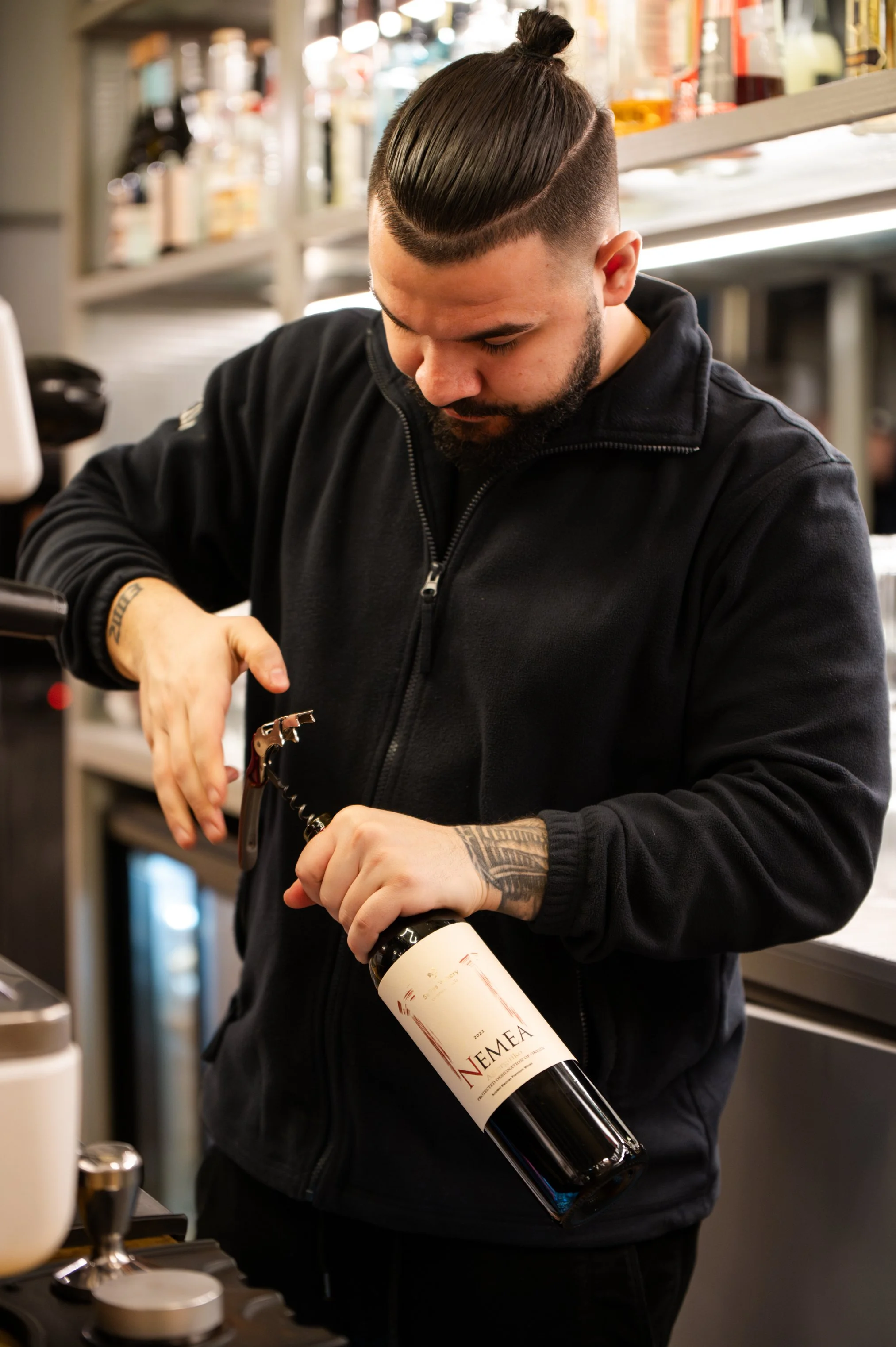 Man opening a bottle of Nemeea wine in a store or bar.