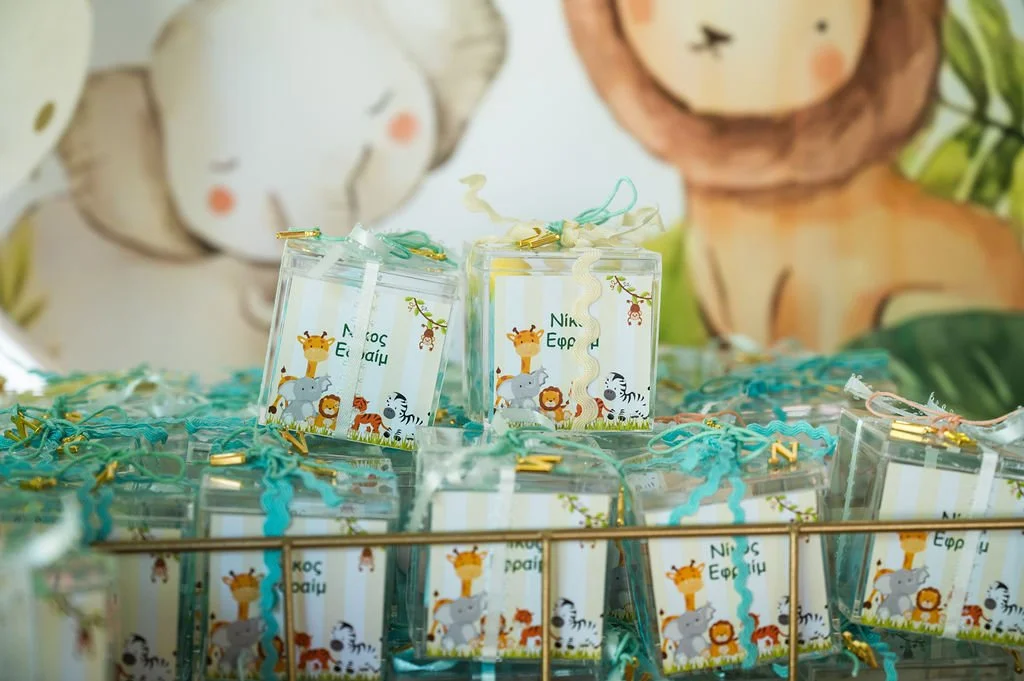 Clear plastic gift boxes with jungle animal designs, tied with turquoise and white ribbons, displayed on a gold wire tray with a colorful jungle-themed background.