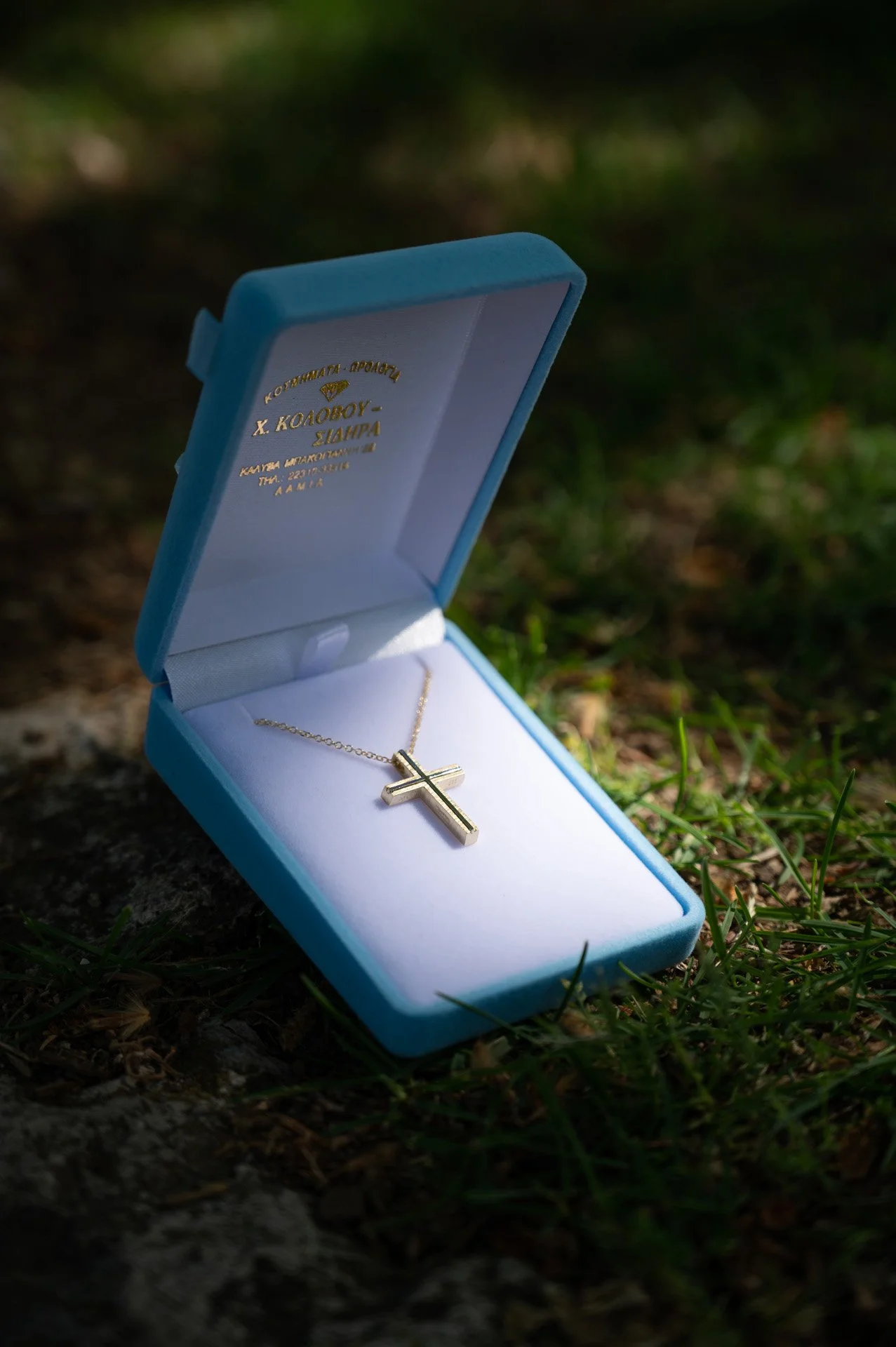 A gold cross necklace inside a light blue jewelry box on the grass.