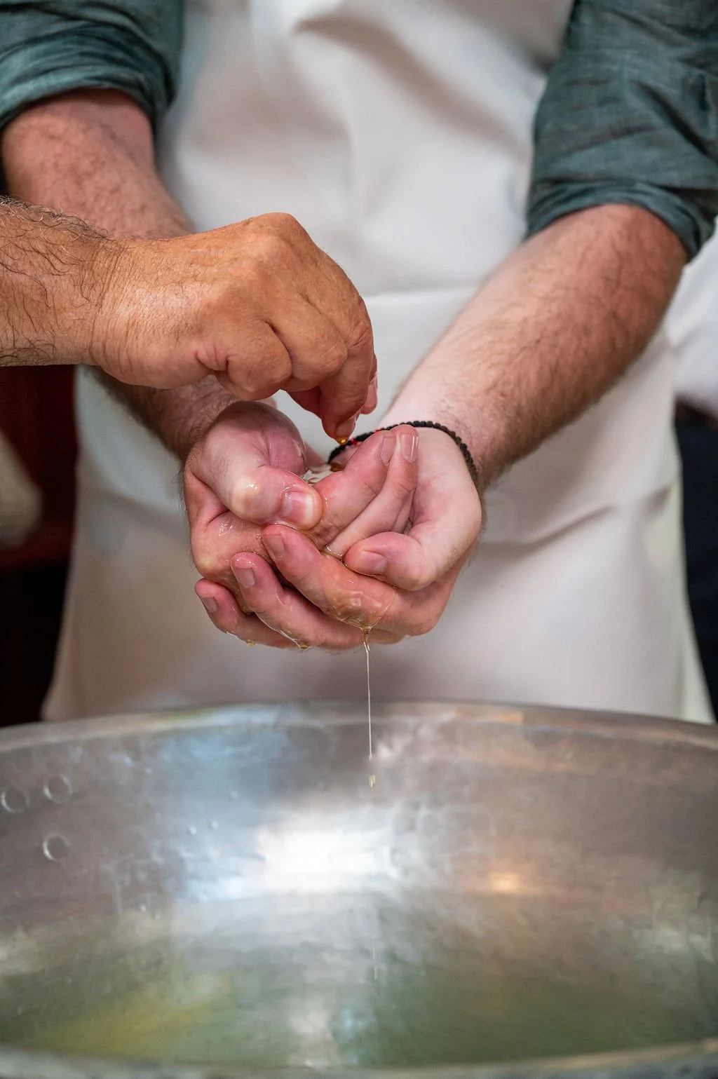 Close-up of a person cracking an egg with two hands over a metal bowl in a kitchen setting.