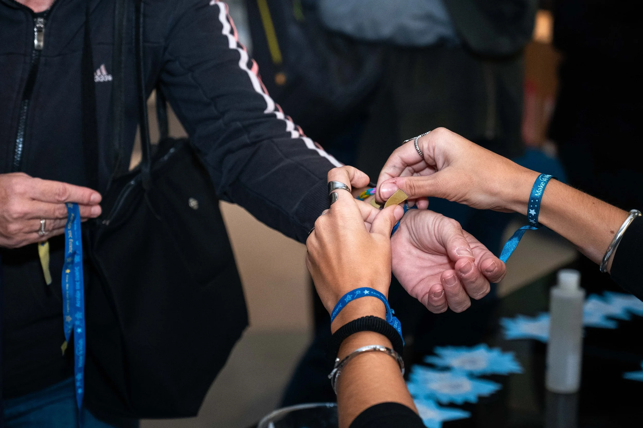 Person wrapping a bracelet on another person's wrist at an event table with wristbands and a small bottle of sanitizer in the background.