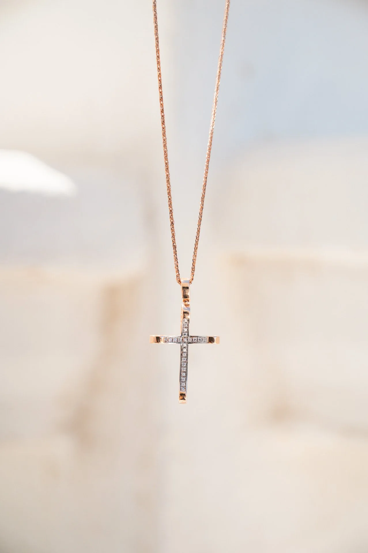 A gold cross necklace with embedded small diamonds hanging from a thin gold chain.