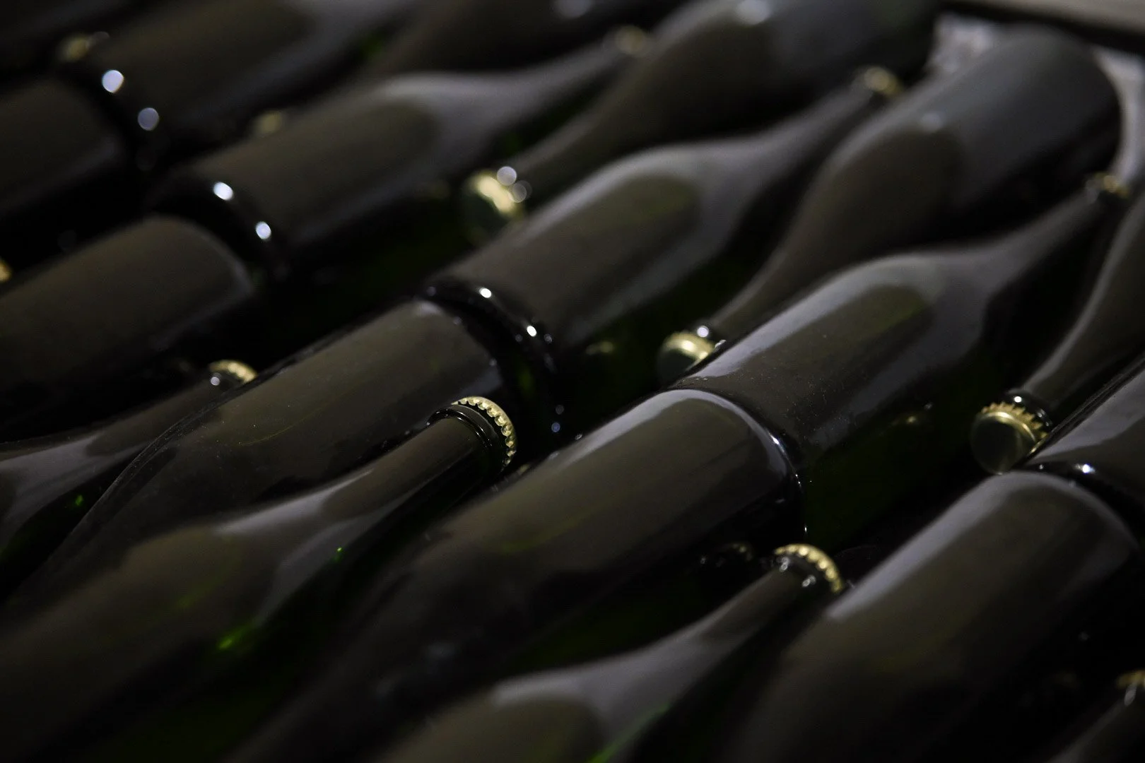 Close-up of multiple empty wine bottles lying horizontally, with their necks and caps visible.