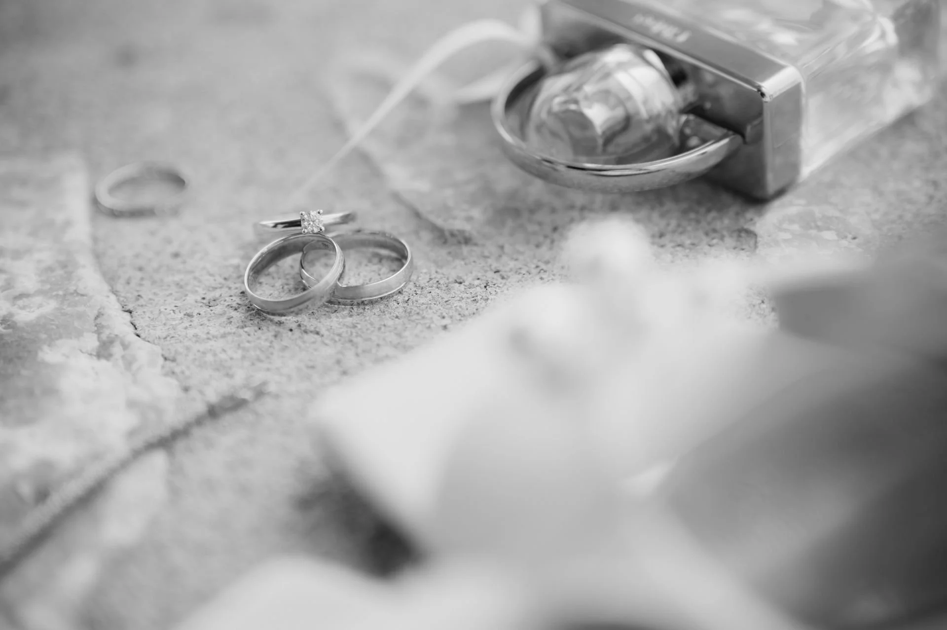 Black and white photograph of wedding rings, one with a diamond, near a box of dental floss on a textured surface.