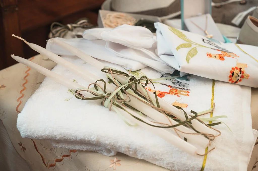 Unbowed white towels, candles tied together with ribbon, embroidered napkin with floral design, and assorted miscellaneous items on a table.