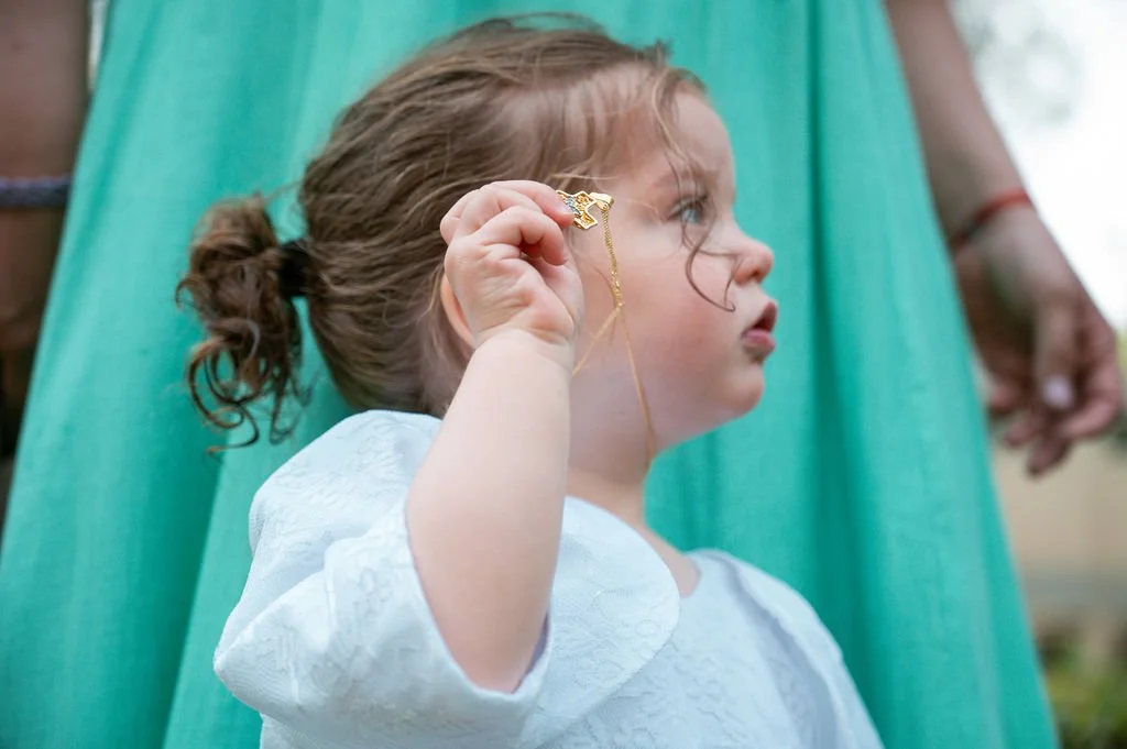 Young girl holding a gold necklace with a star pendant, looking to the side, with a woman in a green dress standing behind her.