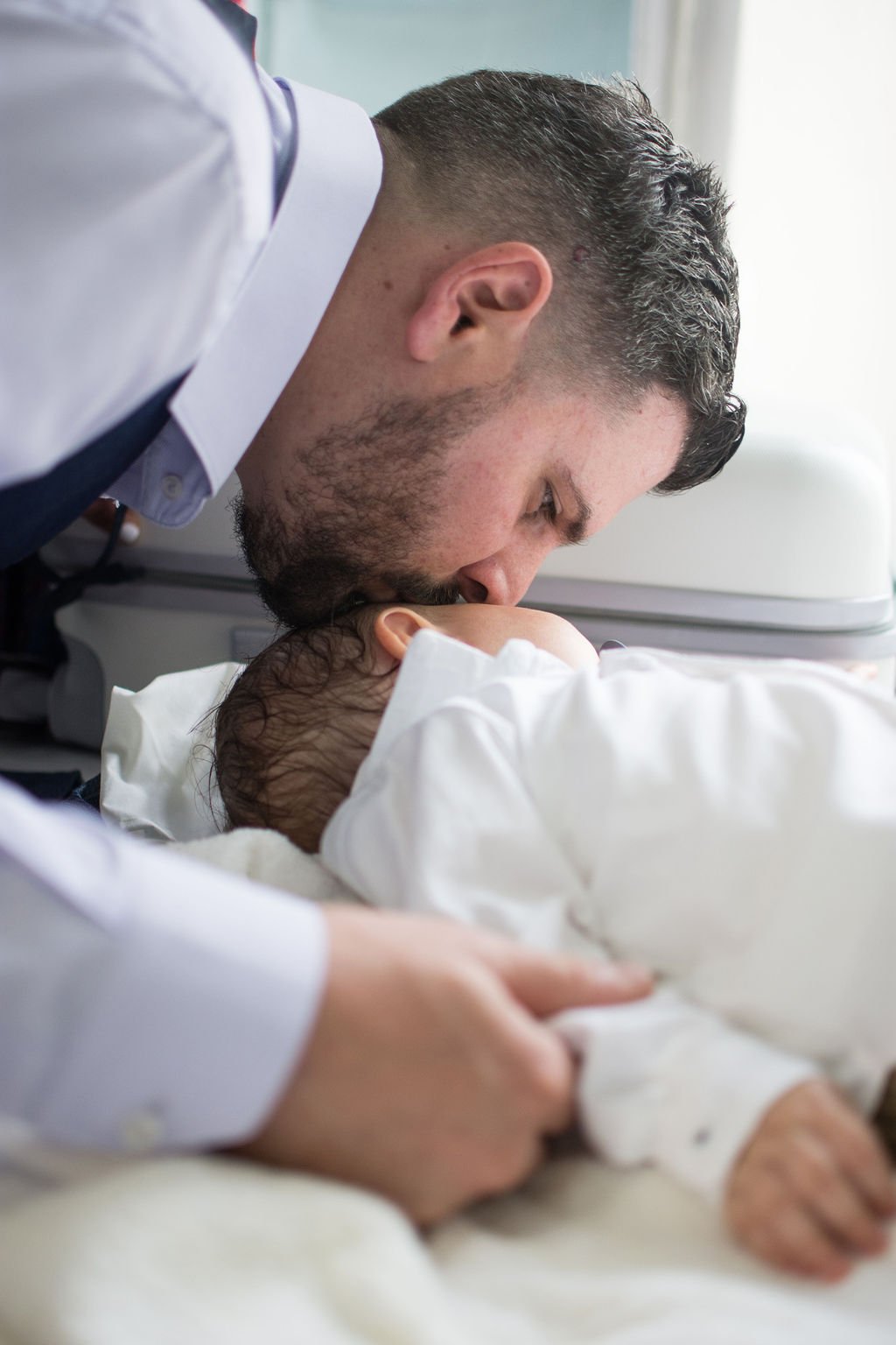 A man leaning over a hospital bed, kissing a newborn baby.