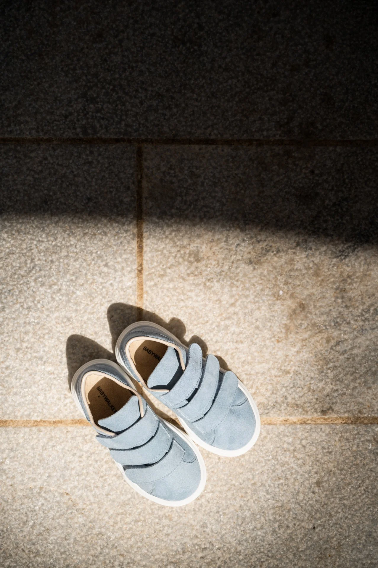 Pair of light blue sneakers on a tiled floor with shadow of the shoes.