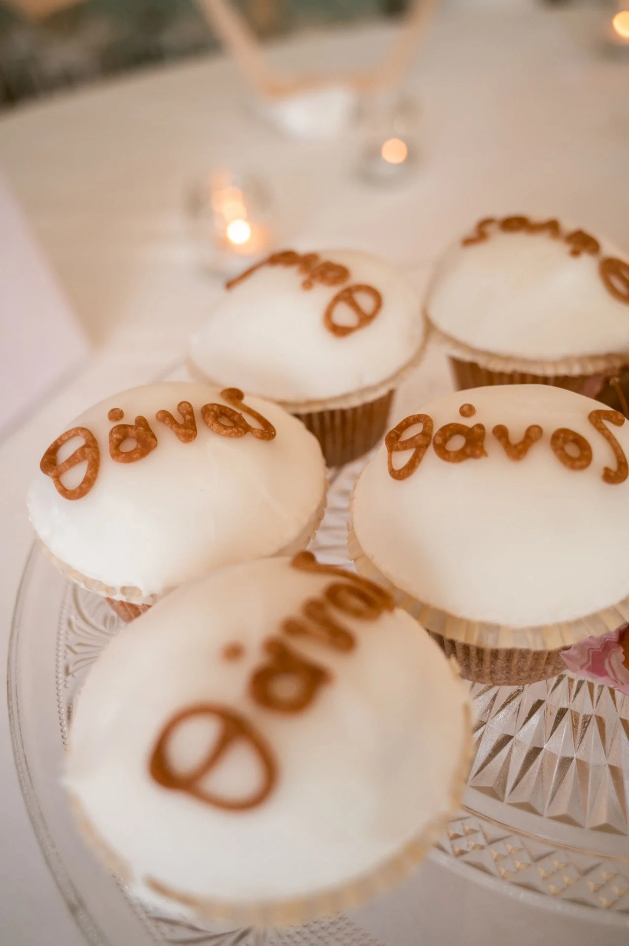 Cupcakes with white frosting decorated with the word 'davs' written in pretzel letters on top, arranged on a glass tray with blurred background.