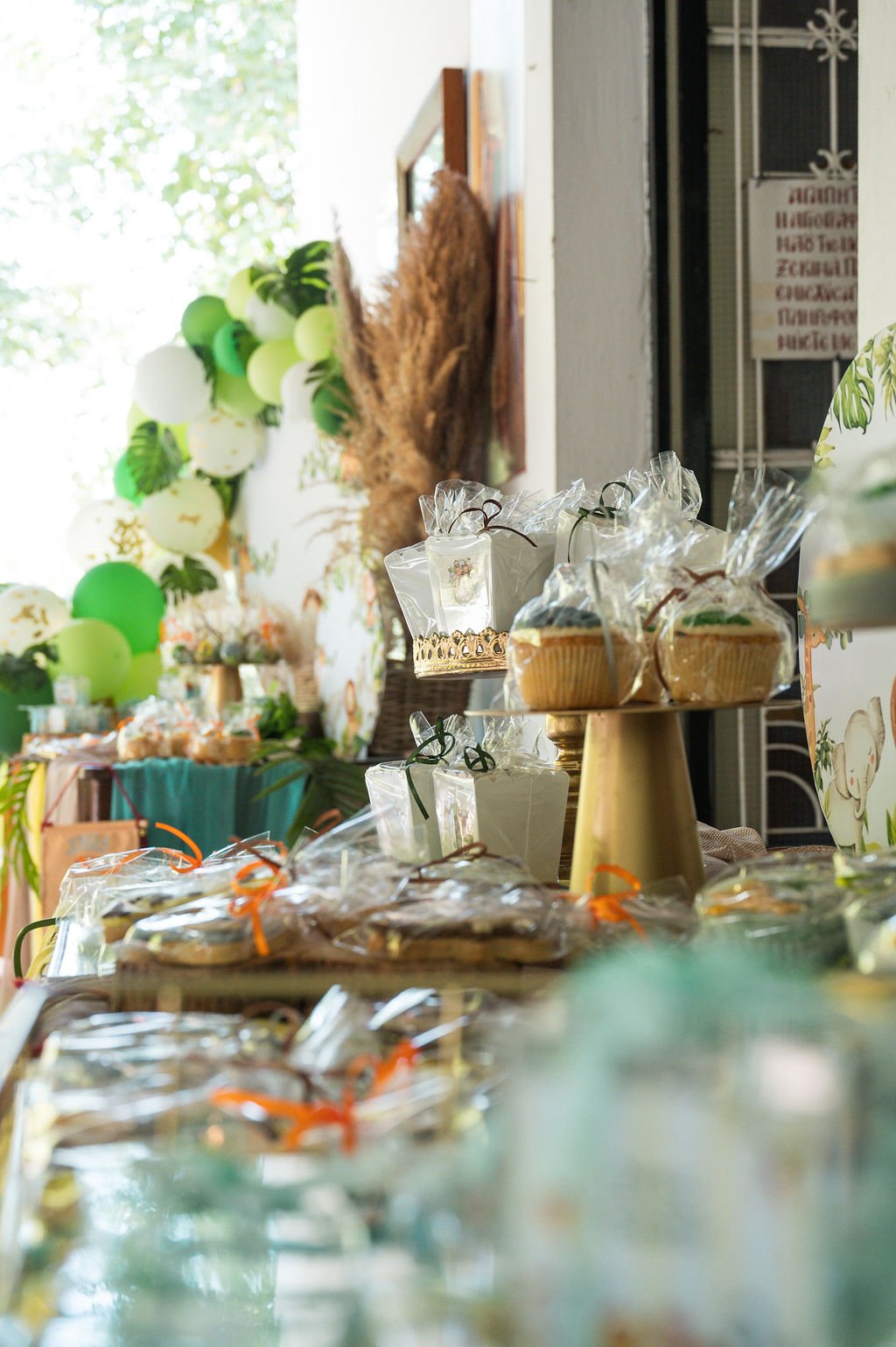 Display of baked goods and treats at a party or celebration, with a backdrop of balloons and decorative leaves.