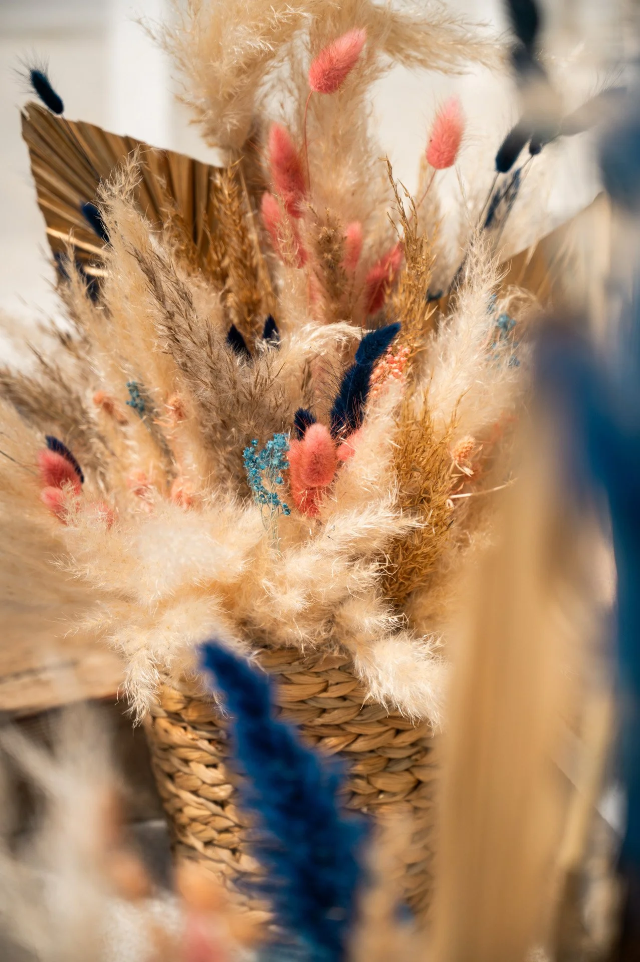 A basket filled with dried decorative plants, including fluffy pampas grass, colorful dried flowers in pink, blue, and beige, arranged for decor.