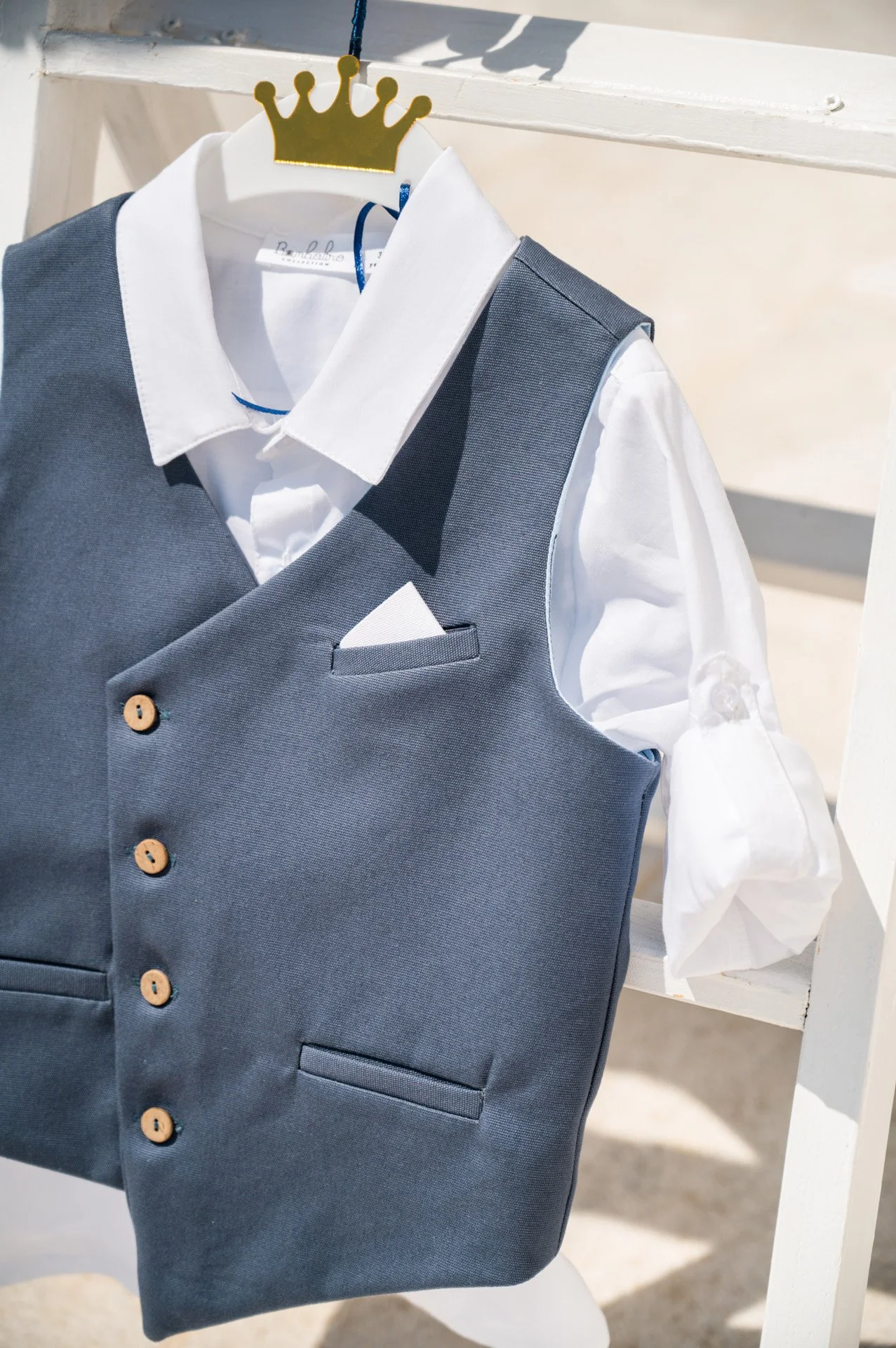 A gray vest and white dress shirt are displayed on a dress form, with a golden crown-shaped hanger.