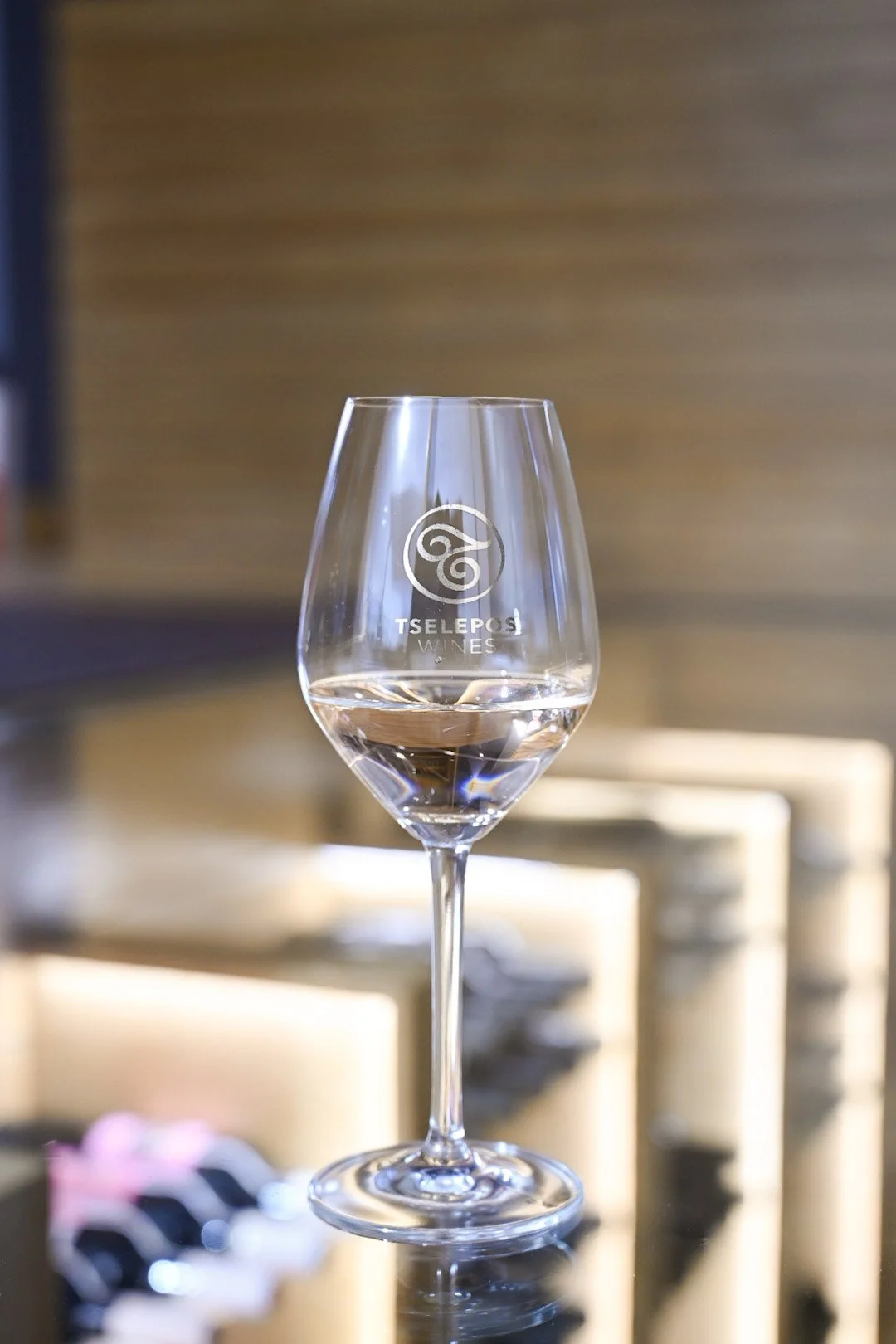 A glass of water on a table with a logo for Tselepos Wines on it, indoors with wooden wall background.