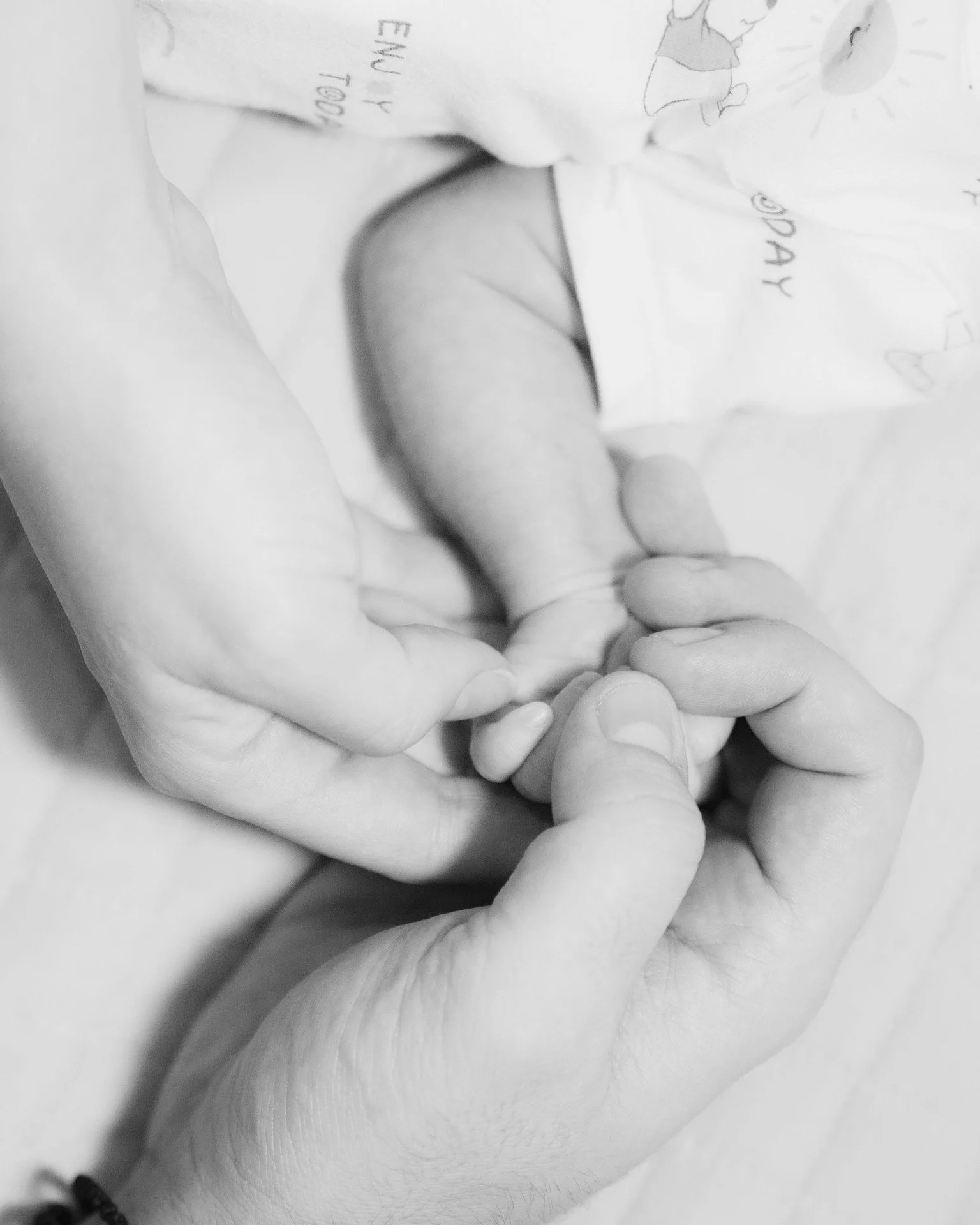 Close-up of an adult hand gently holding a newborn baby's tiny hand.