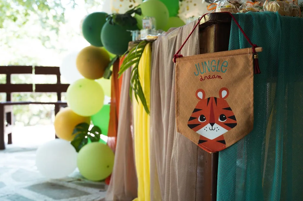 Decorative jungle-themed party setup with colorful balloons, foliage, and a banner featuring a cute tiger illustration with the text "Jungle Dream."