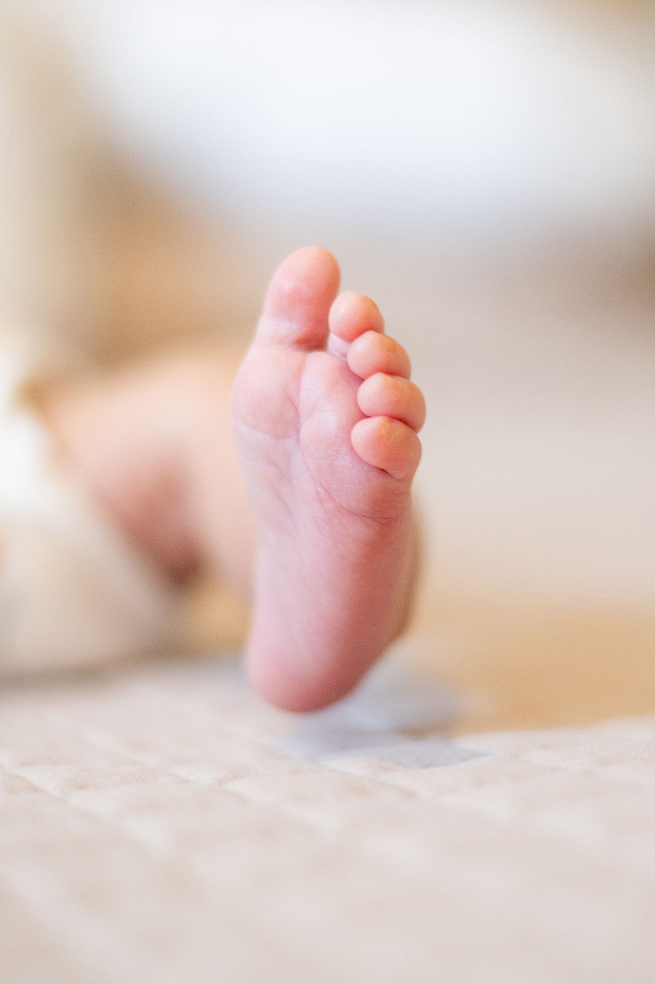 Close-up of a tiny baby foot with curled toes resting on a soft surface.