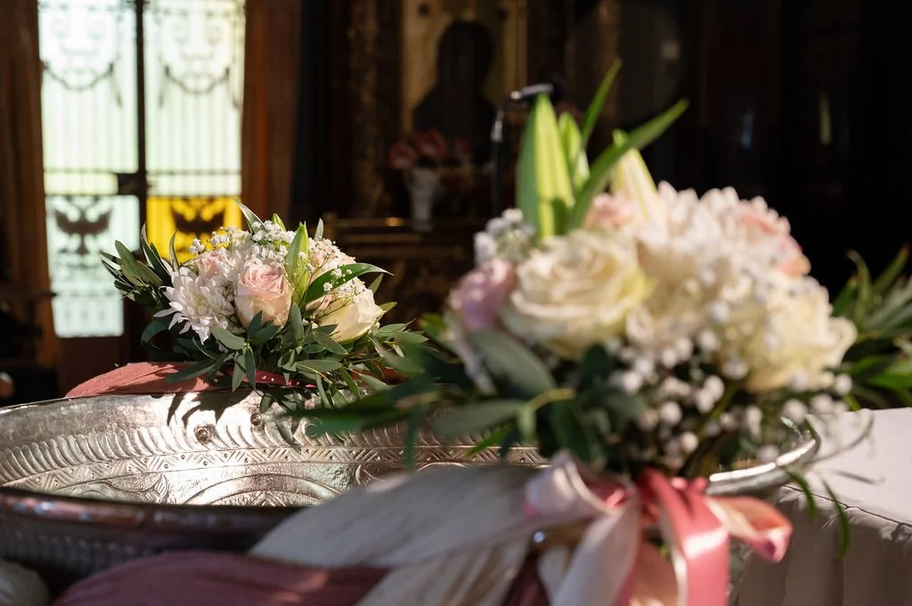 Close-up of floral arrangements with white and pink flowers, greenery, and pink ribbon decorations on a table.