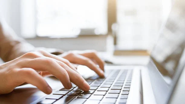 Close-up of hands typing on a laptop keyboard in a well-lit room.