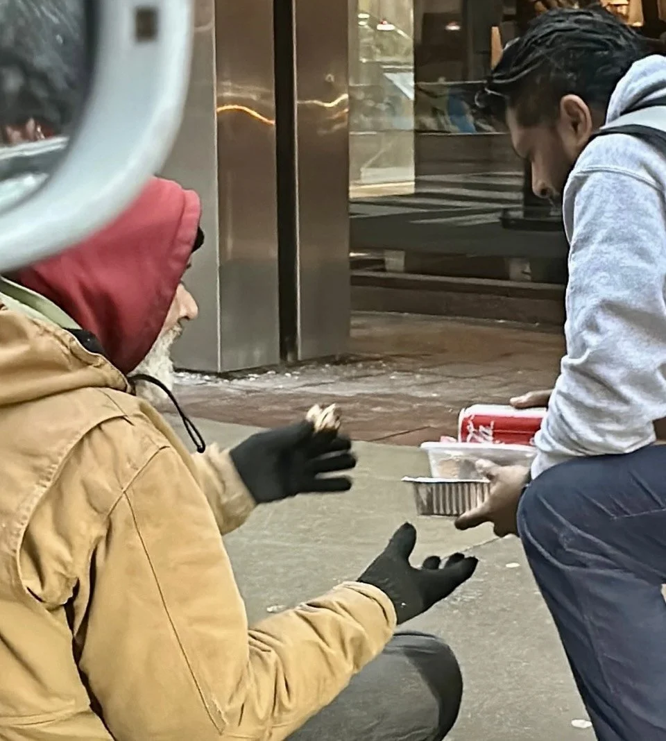 homeless-man-sitting-on-sidewalk-in-winter-receiving-free-meal-from-RN